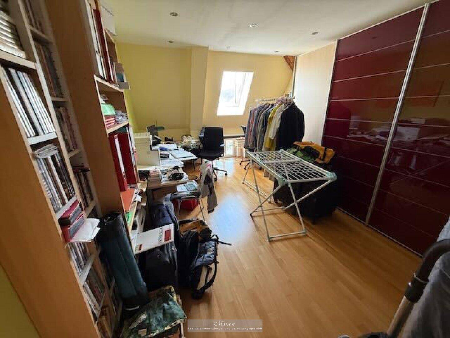 Funktionales Arbeitszimmer im Dachgeschoss mit Schreibtisch, Regal und Dachfenster.