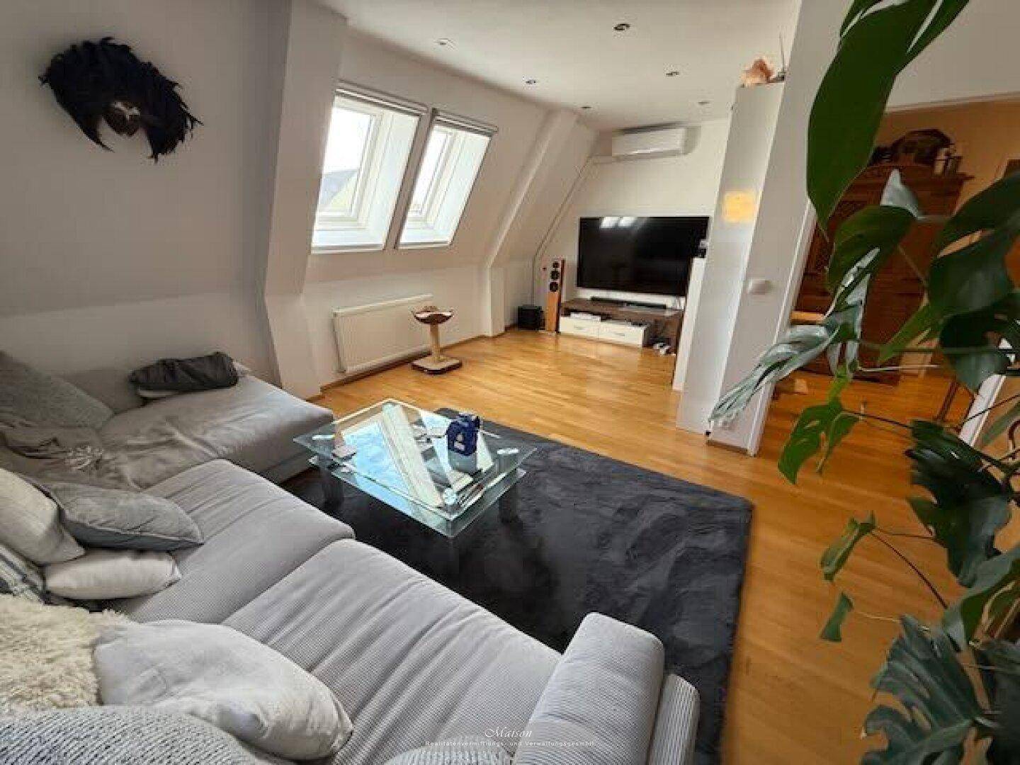 Helles Dachgeschoss-Wohnzimmer mit großem Sofa, Fernseher und Klimaanlage.