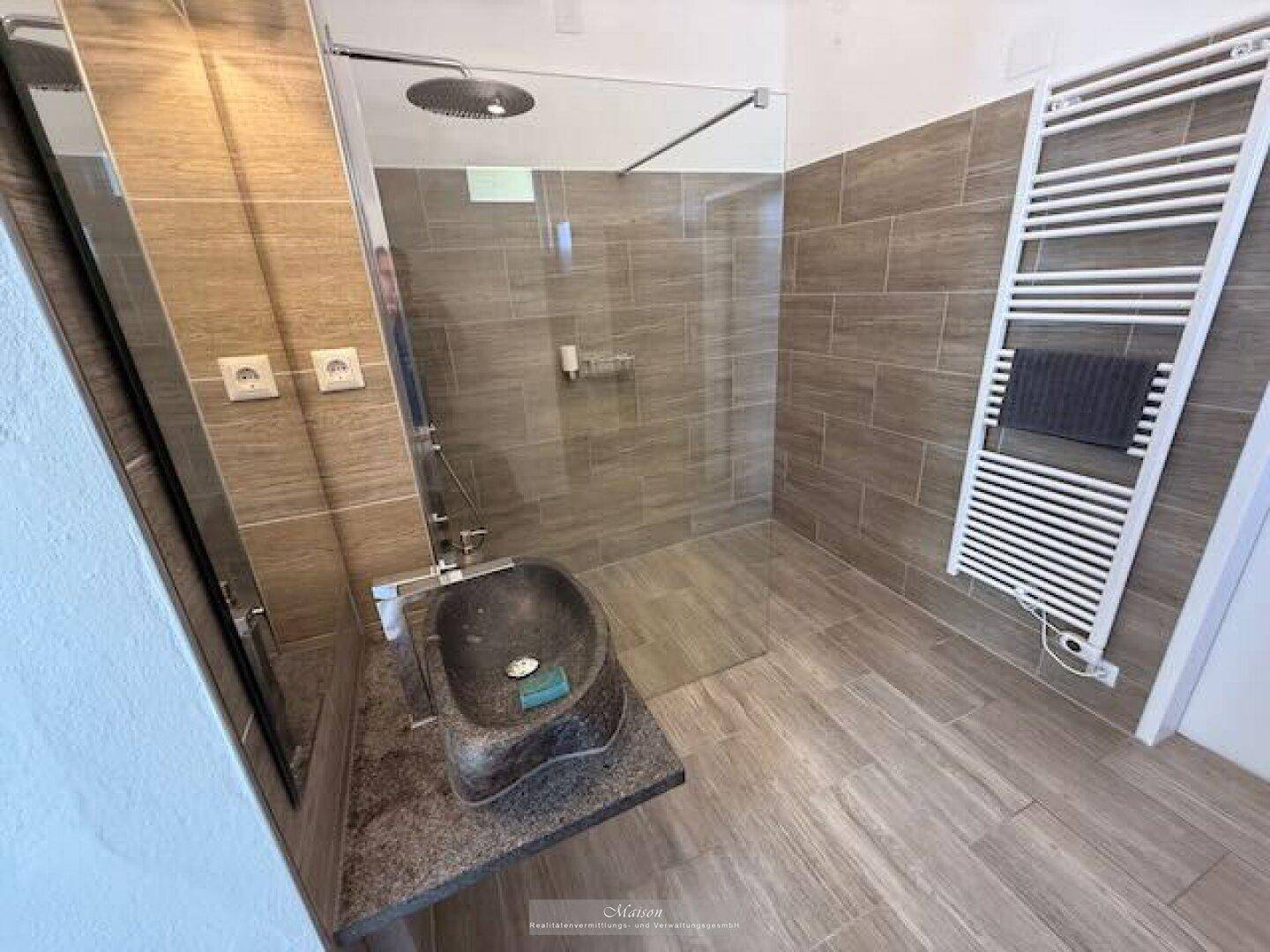 Modernes Badezimmer mit begehbarer Dusche, Natursteinwaschbecken und beheiztem Handtuchhalter.