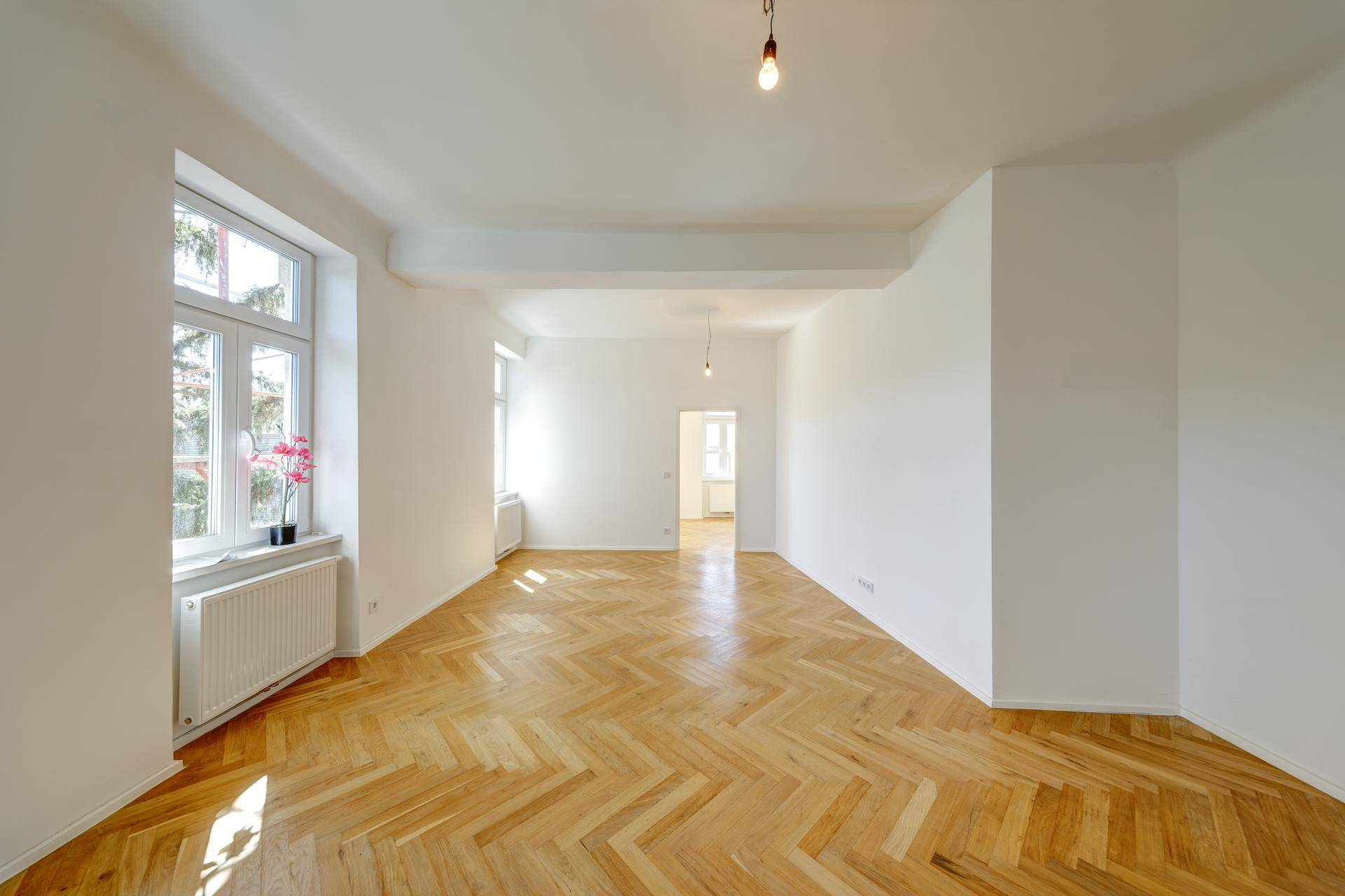 Geräumiges Wohnzimmer mit Fischgrätparkett und viel Tageslicht durch die Fenster.