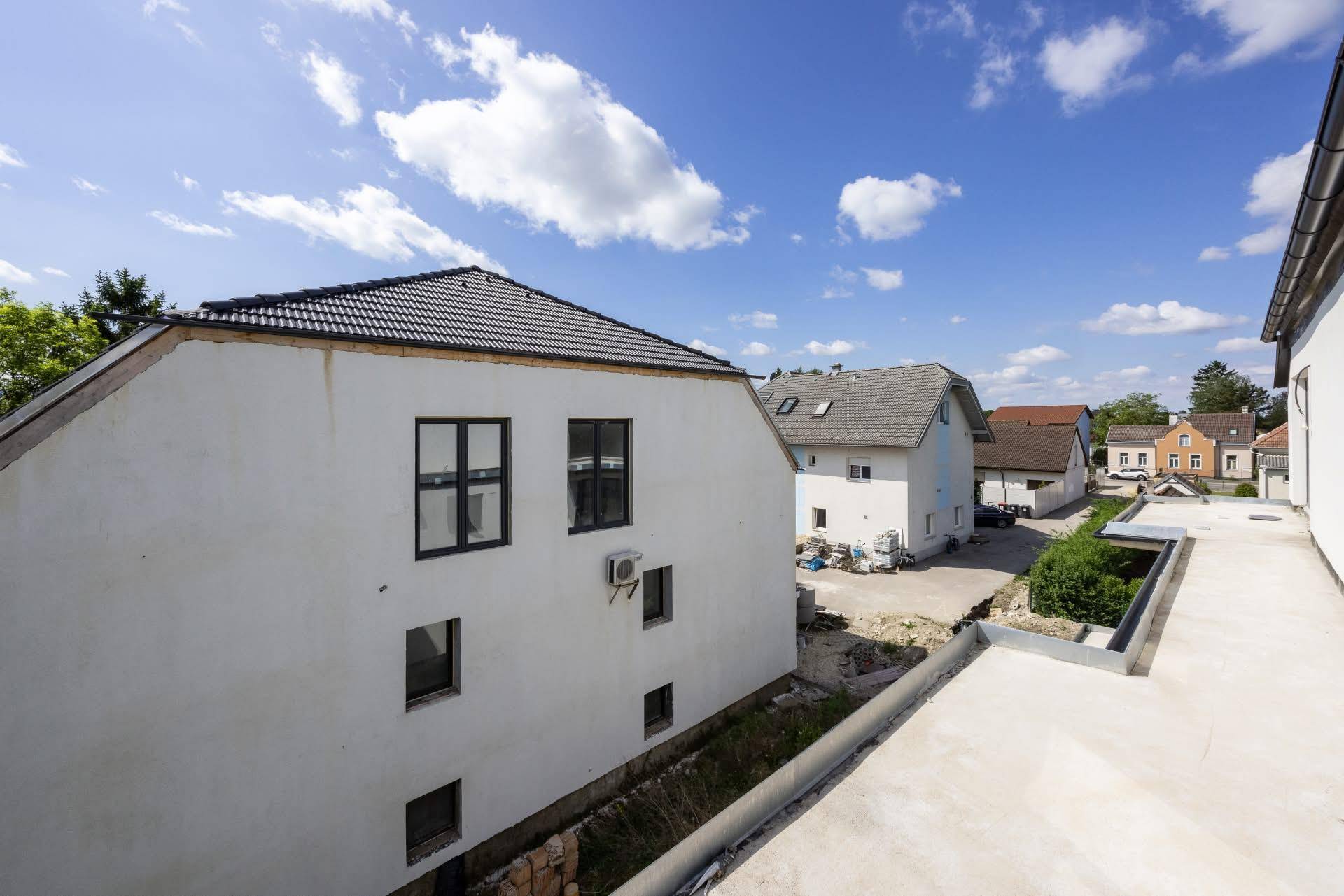 Rückansicht eines Neubaus mit Dachterrasse und Blick auf die umliegende Wohngegend.
