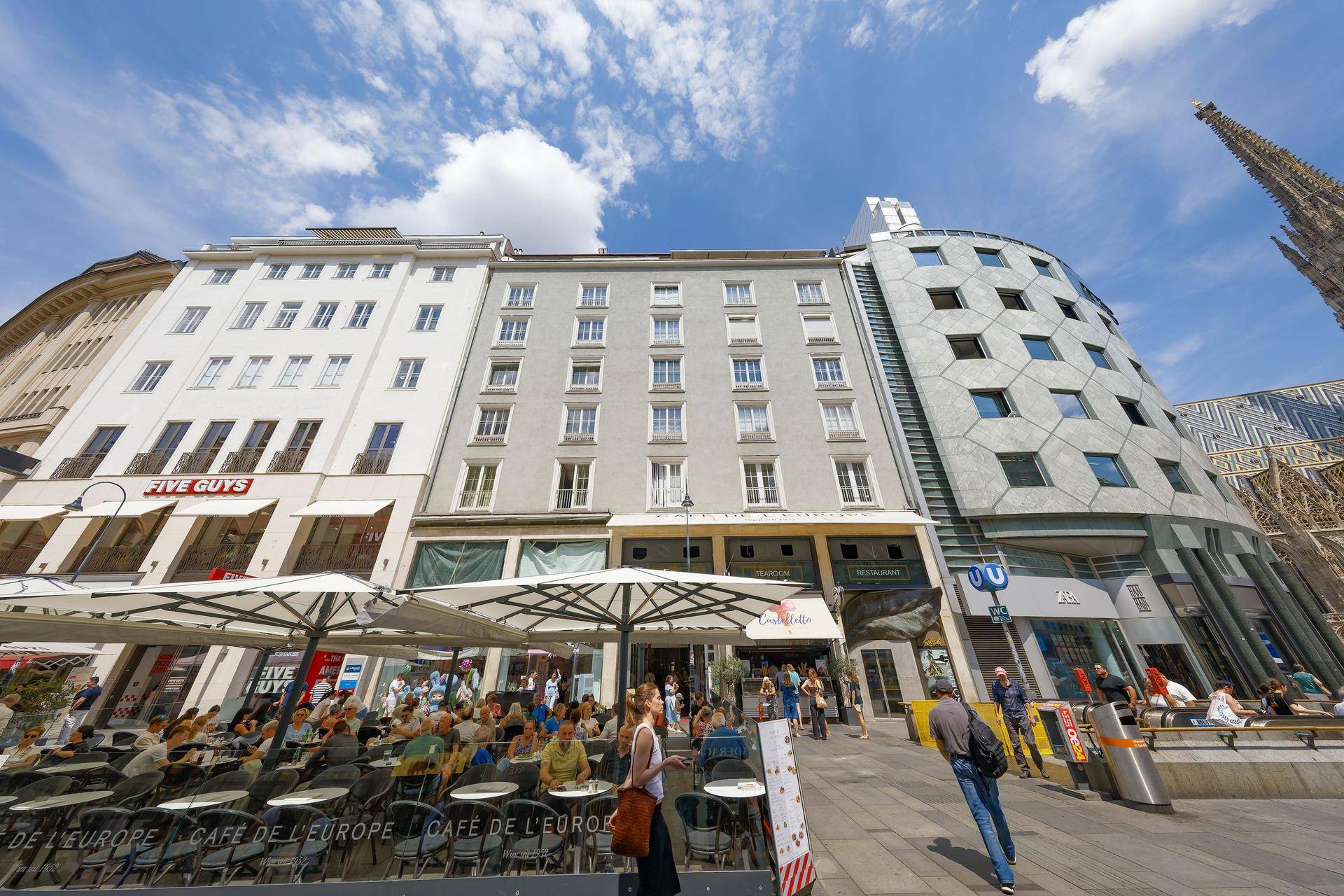 Fassadenansicht der Gebäude am belebten Stadtplatz mit moderner Architektur und blauem Himmel.