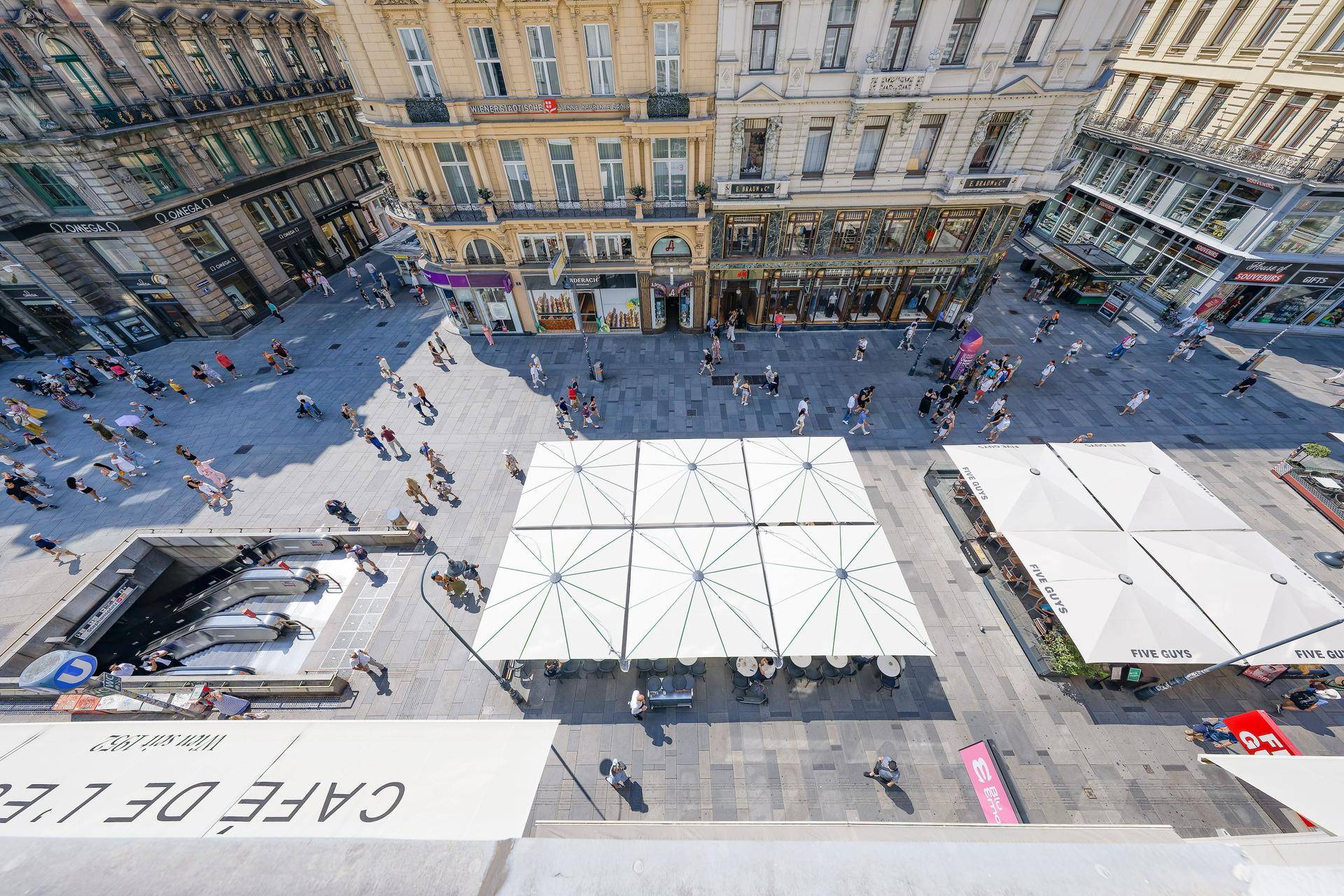 Blick von oben auf den belebten Stadtplatz mit zahlreichen Passanten und Außengastronomie.