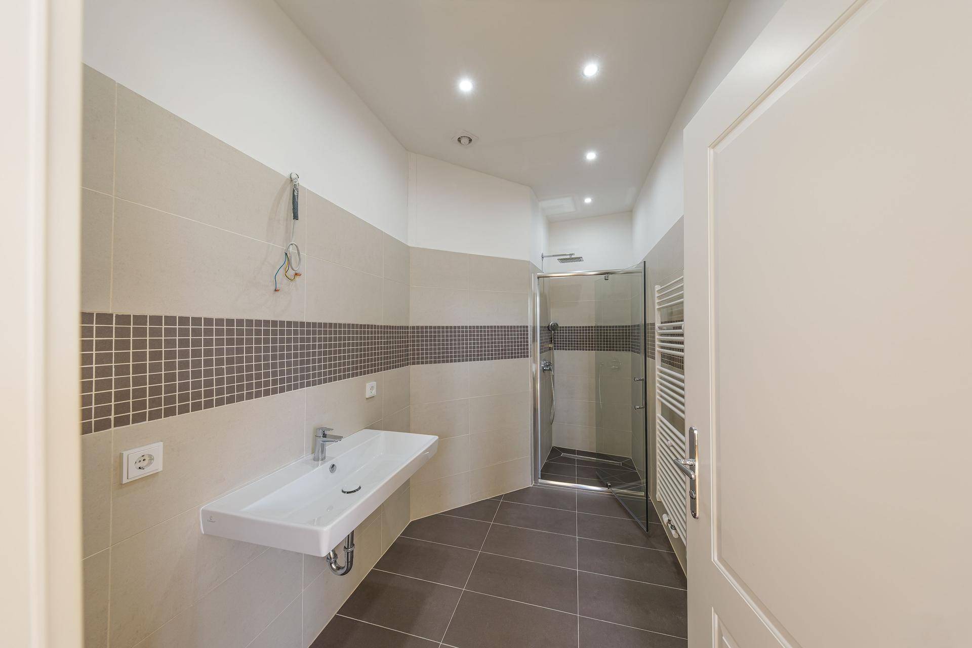 Modernes Badezimmer mit begehbarer Dusche, eleganten Fliesen und einem einzelnen Waschbecken.
