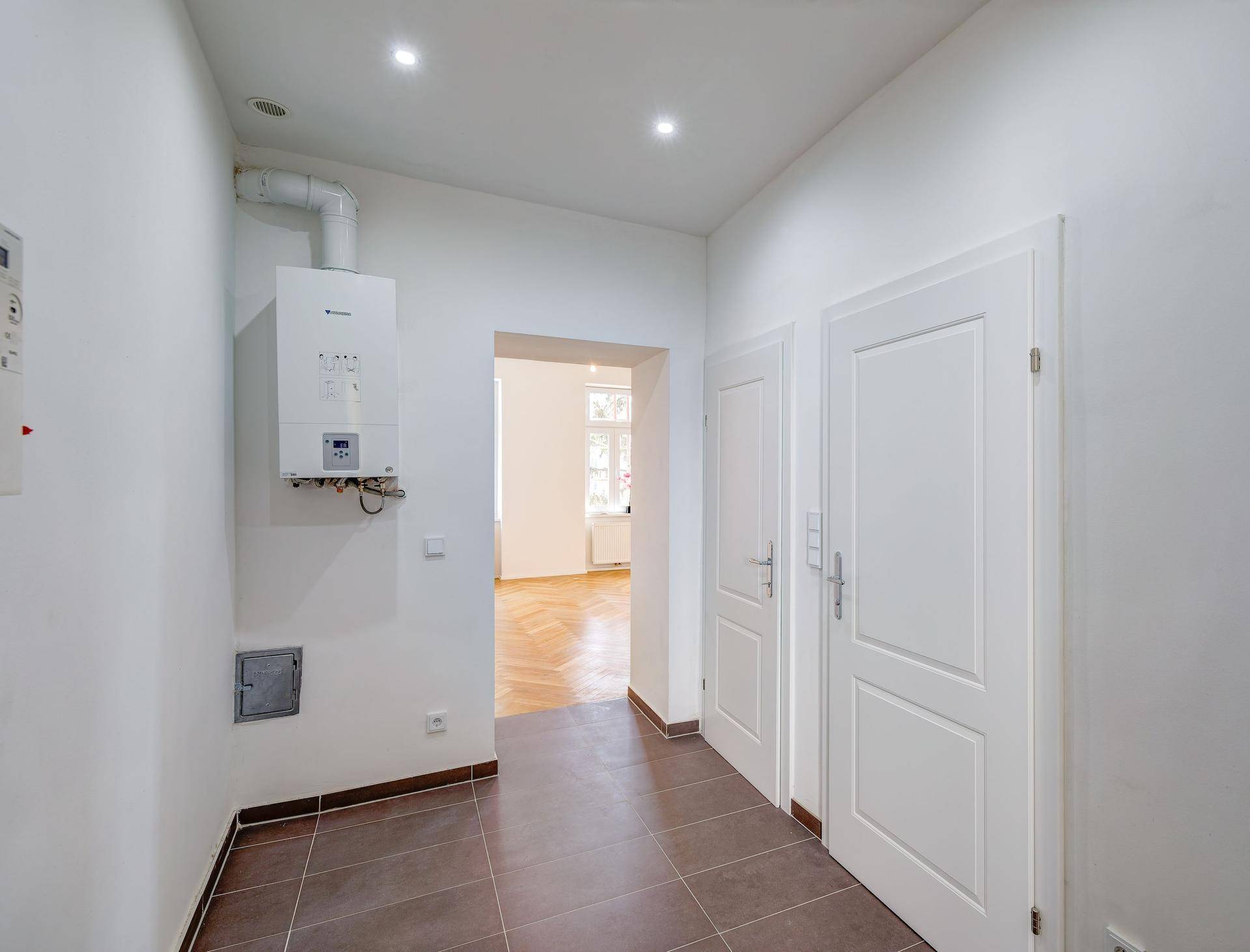 Heller Flur mit Fliesenboden und Gastherme, der zu weiteren Zimmern der Wohnung führt.