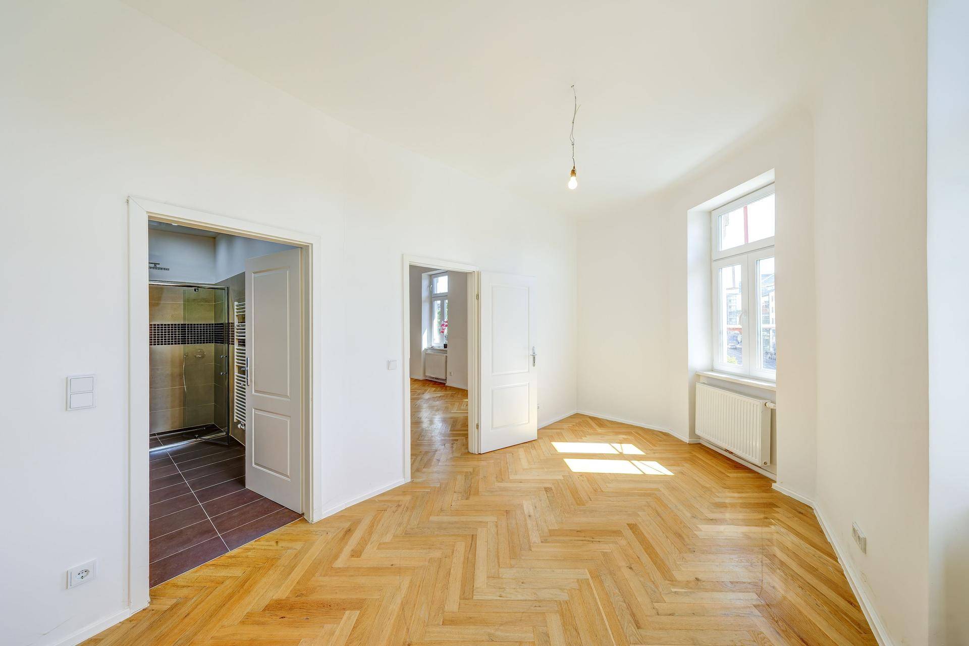 Helles Zimmer mit Fischgrätparkett und direktem Zugang zu einem modernen Badezimmer.