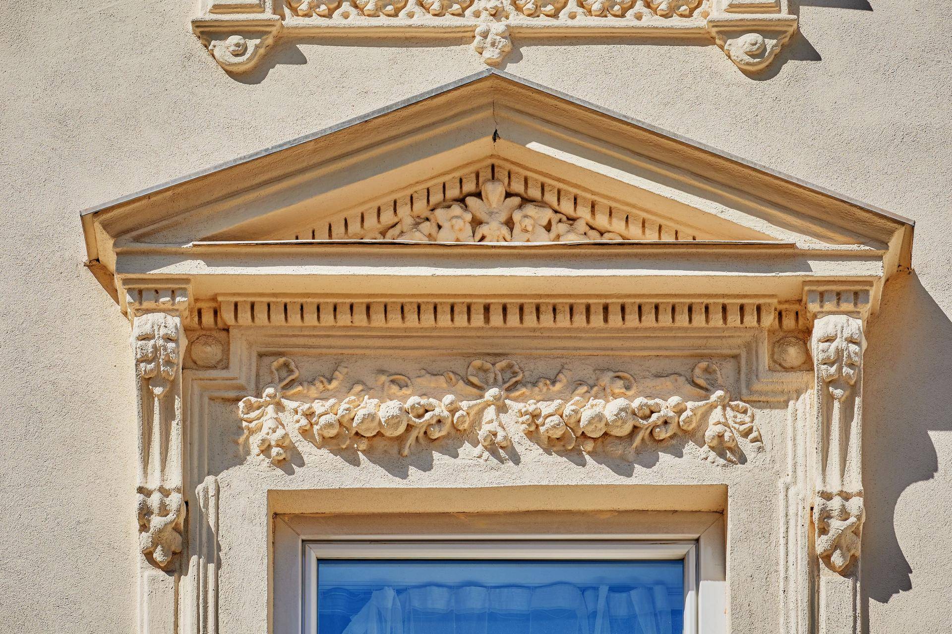 Nahaufnahme der aufwendigen Stuckverzierungen über einem Fenster der historischen Fassade des Gebäudes.