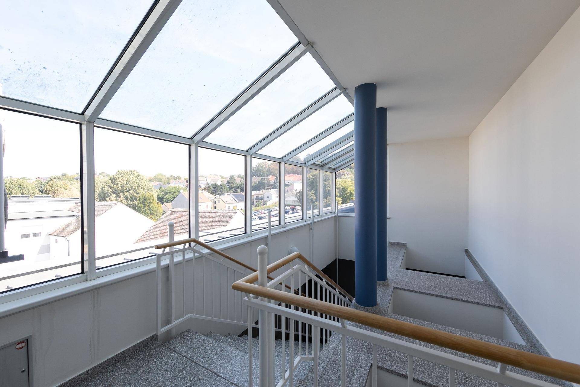 Lichtdurchflutetes Treppenhaus mit großflächiger Glasüberdachung und Blick auf die Umgebung.