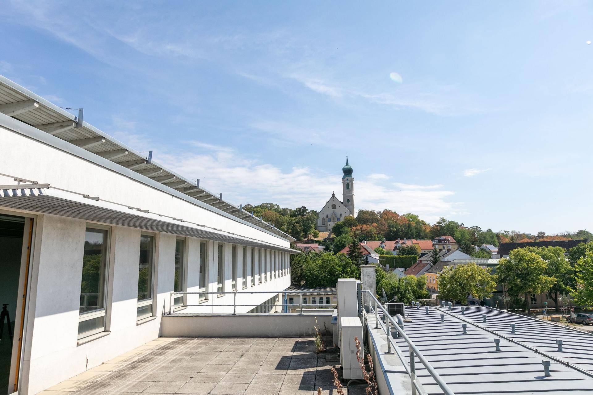 Große Dachterrasse mit weitem Blick über die Stadt und eine Kirche im Hintergrund.