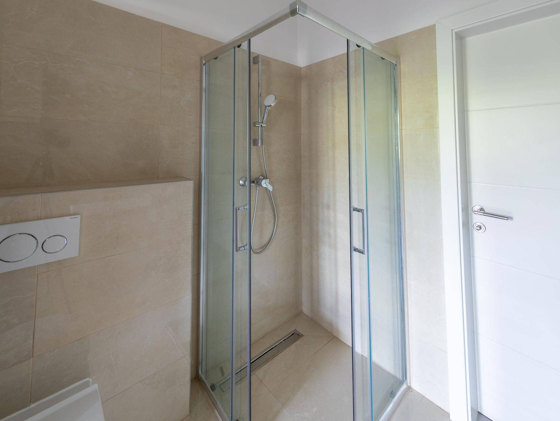 Modernes Badezimmer mit begehbarer Dusche, beigefarbenen Fliesen und wandhängendem WC.