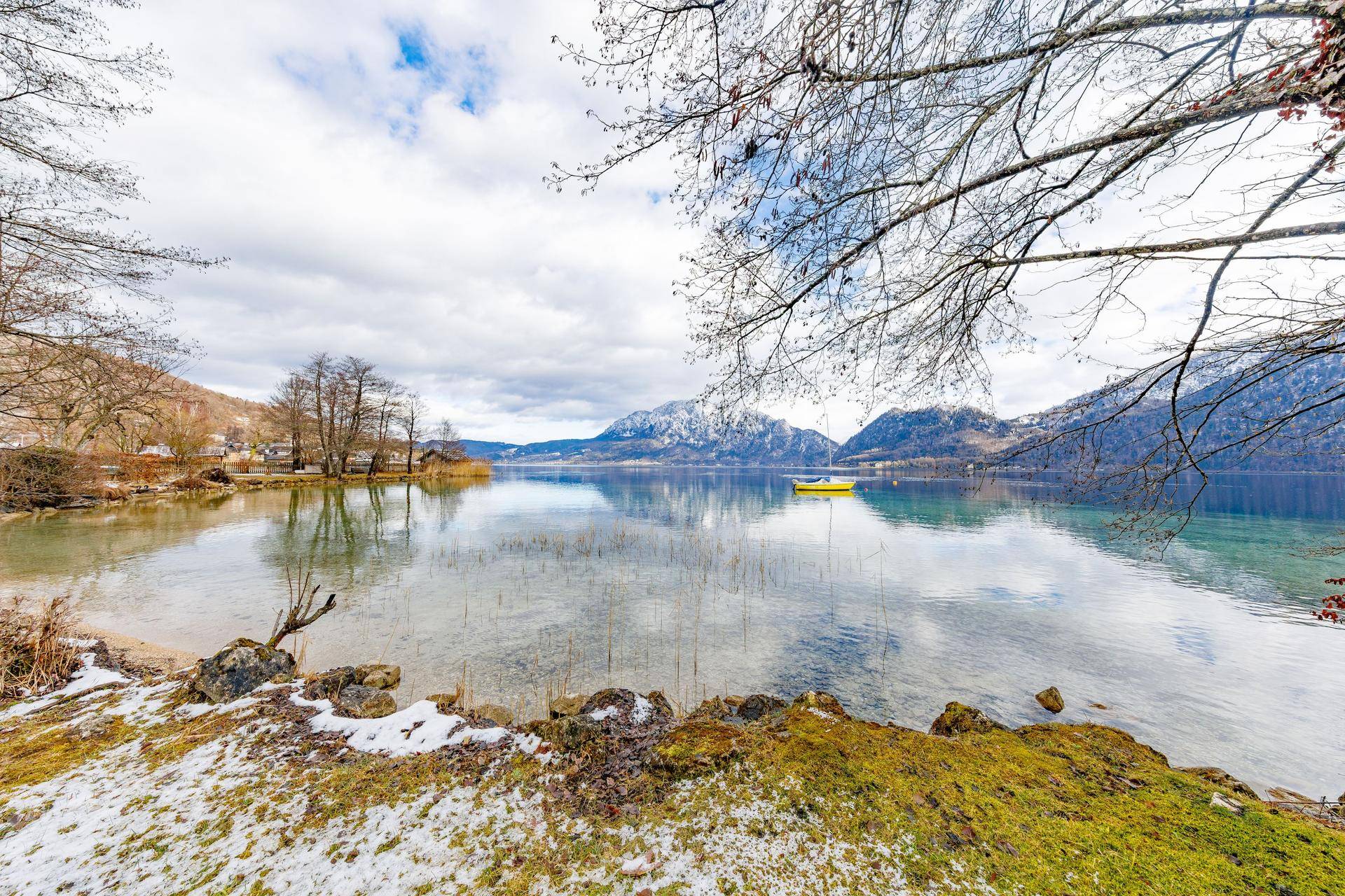 Idyllischer Blick auf einen ruhigen See mit schneebedeckten Ufern und majestätischen Bergen im Hintergrund.