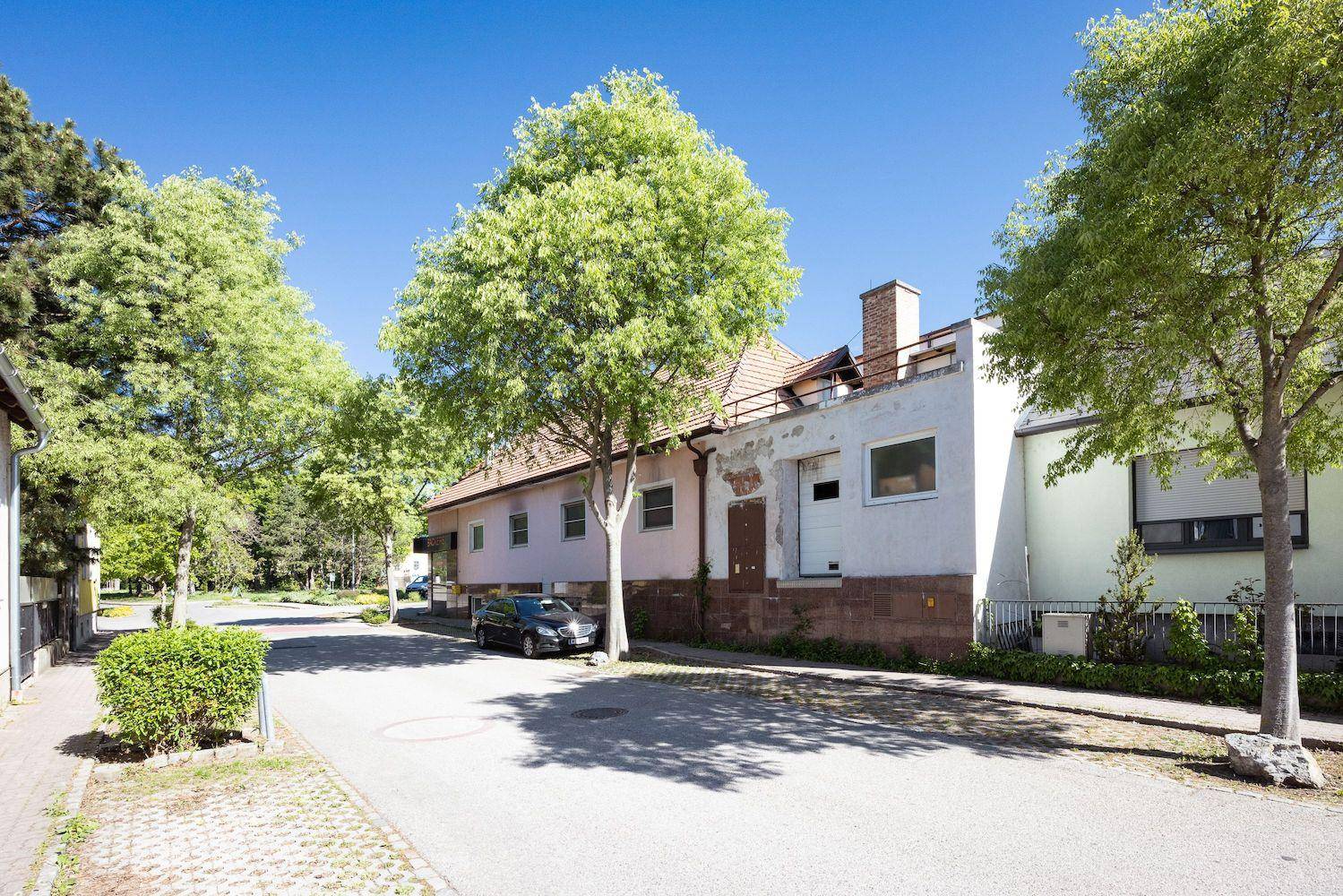Rückseite eines Gebäudes mit einfacher Fassade und einem Auto auf der Straße unter grünen Bäumen.
