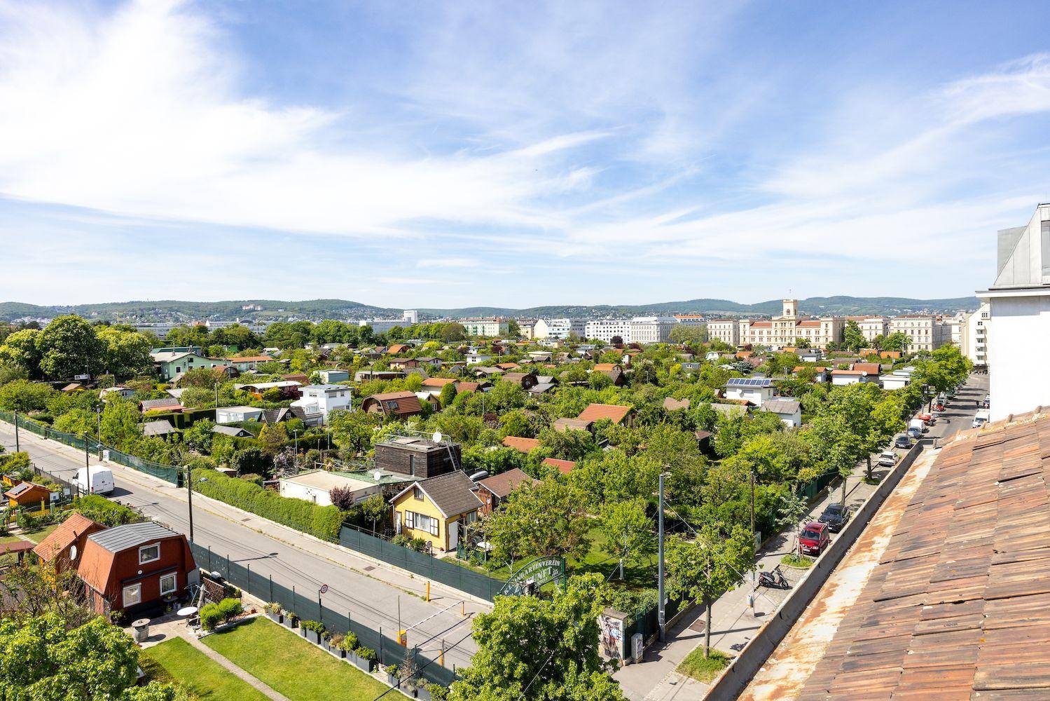 Weitläufiger Blick über eine grüne Wohnsiedlung mit Kleingärten und Hügeln im Hintergrund.