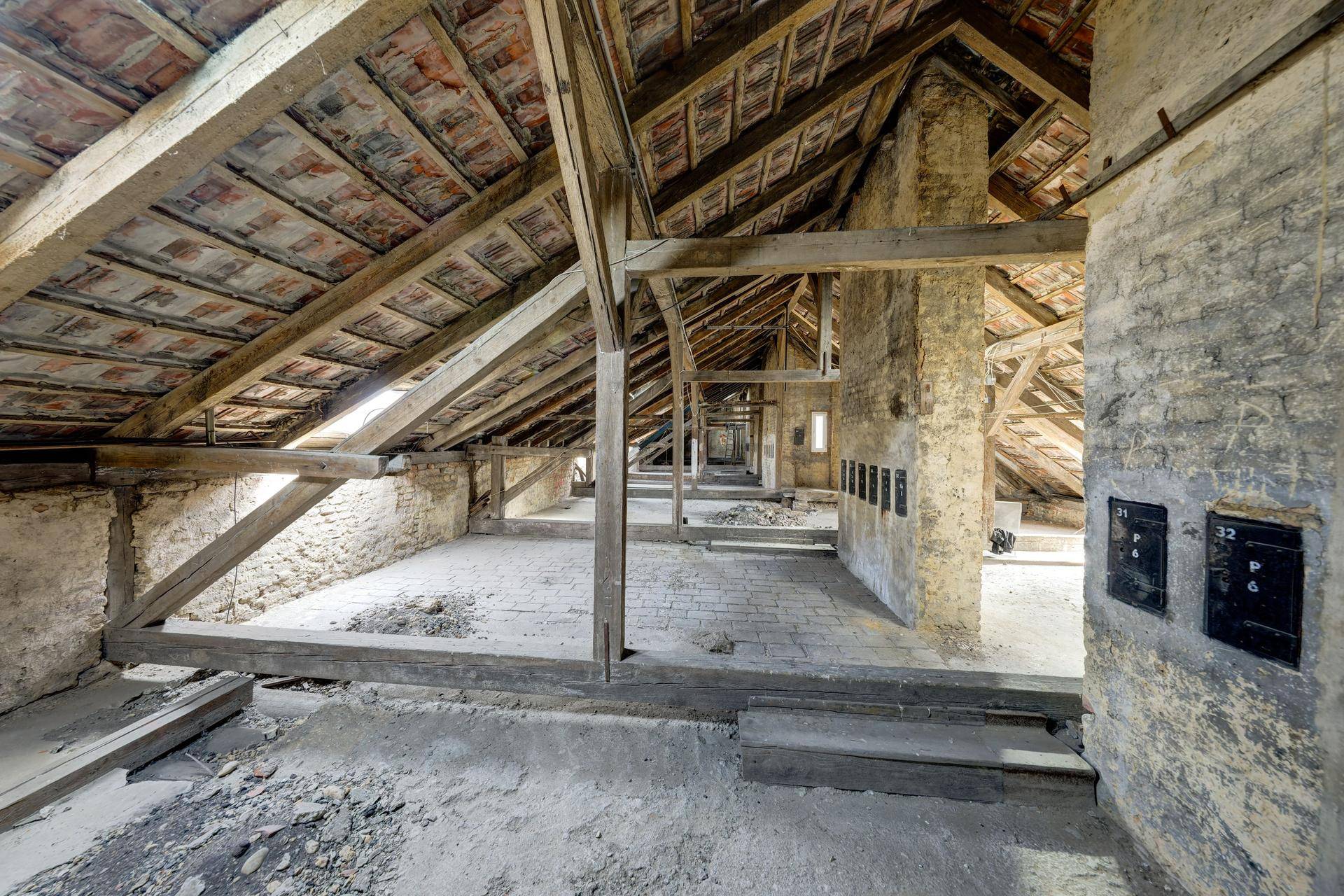 Unausgebauter Dachboden mit sichtbaren Holzbalken und Ziegelboden, bereit für den Ausbau.