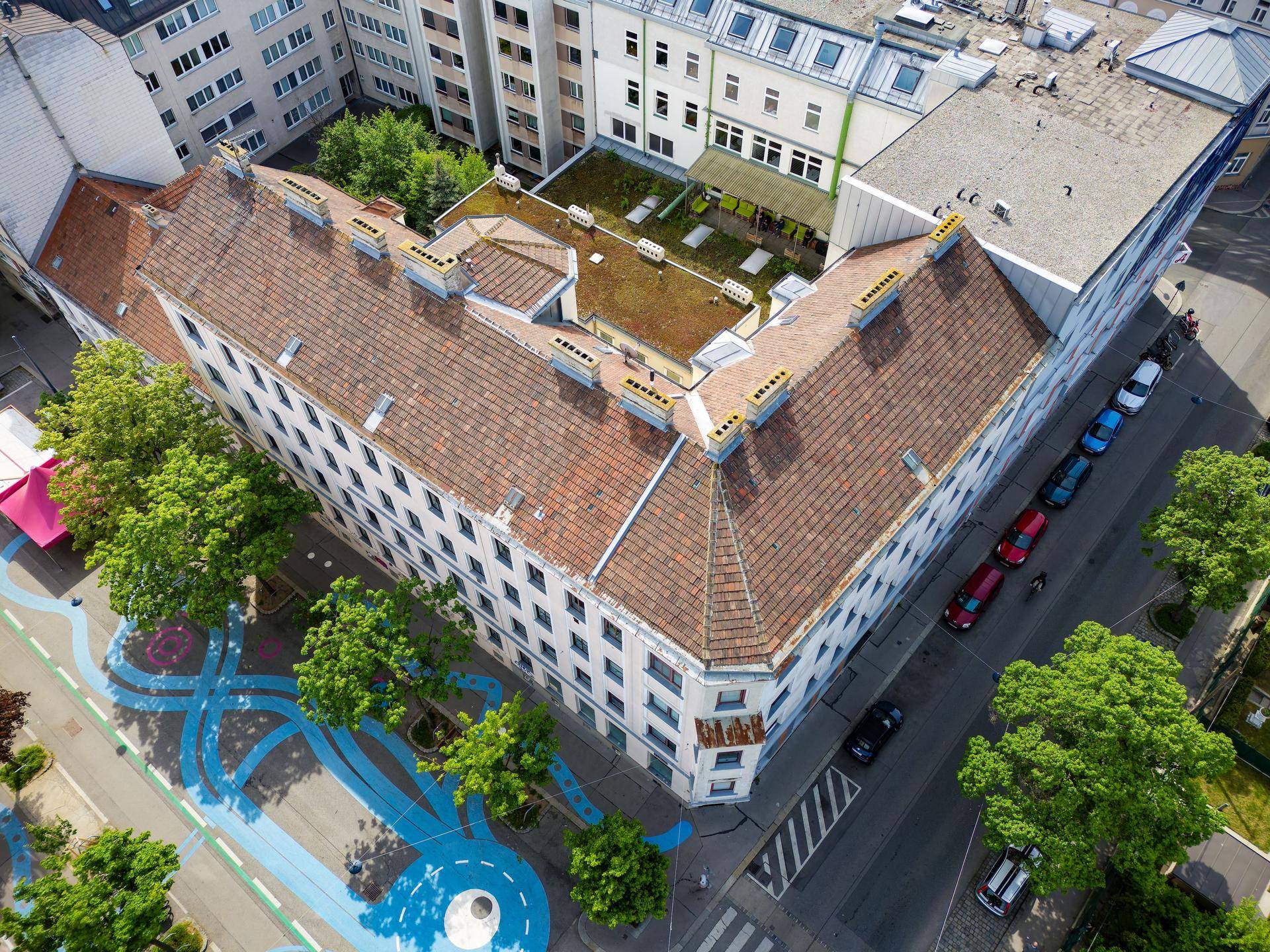 Luftaufnahme des Gebäudes mit traditionellem Ziegeldach und umliegender Stadtlandschaft.