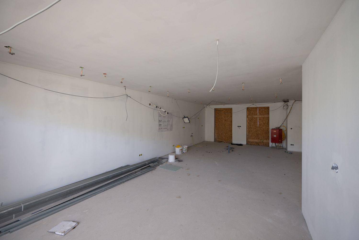 Unfertiger Innenraum mit sichtbaren Installationen und zwei Holztüren, bereit für den Ausbau.