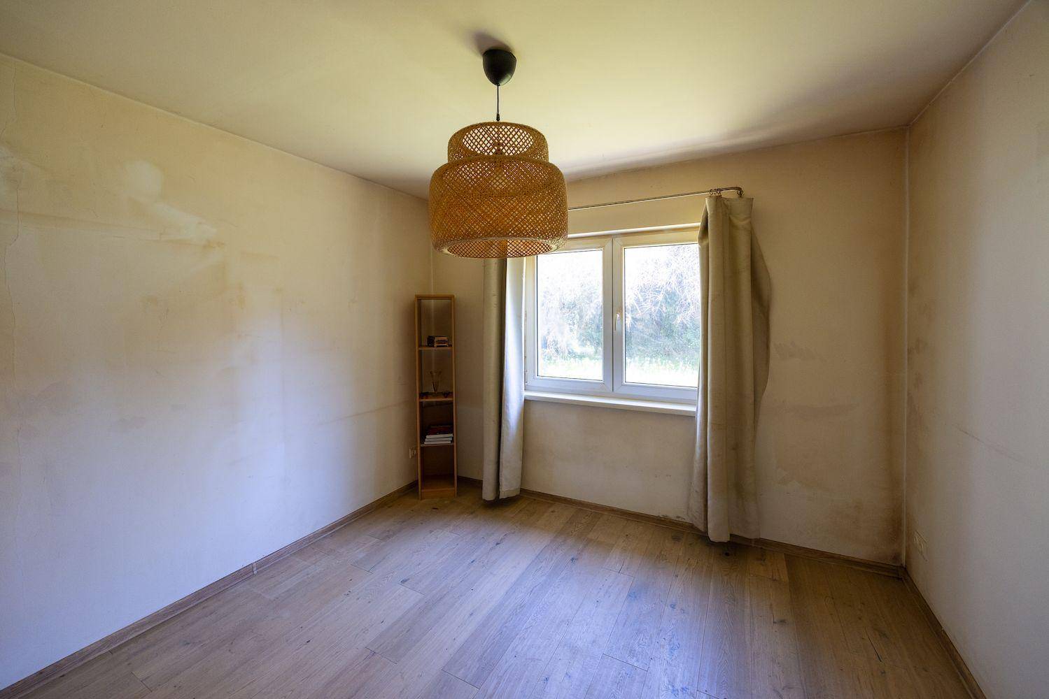 Helles Zimmer mit Laminatboden, einem Fenster und einer modernen Hängelampe.