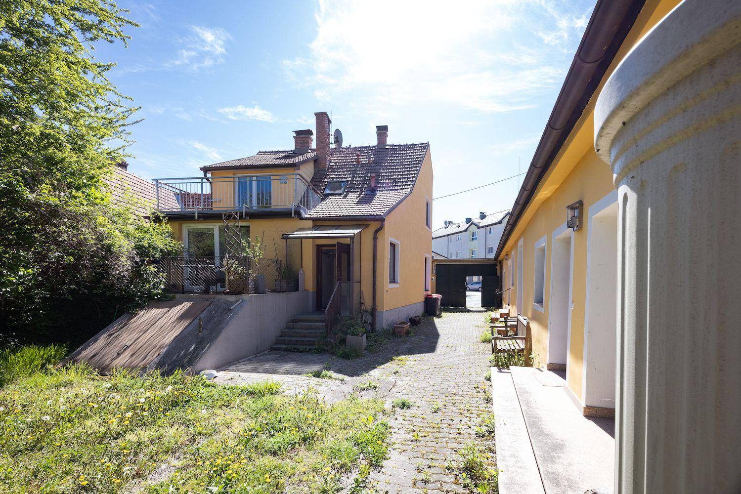Rückansicht des Hauses mit Balkon, gepflastertem Bereich und einem grünen Hang.