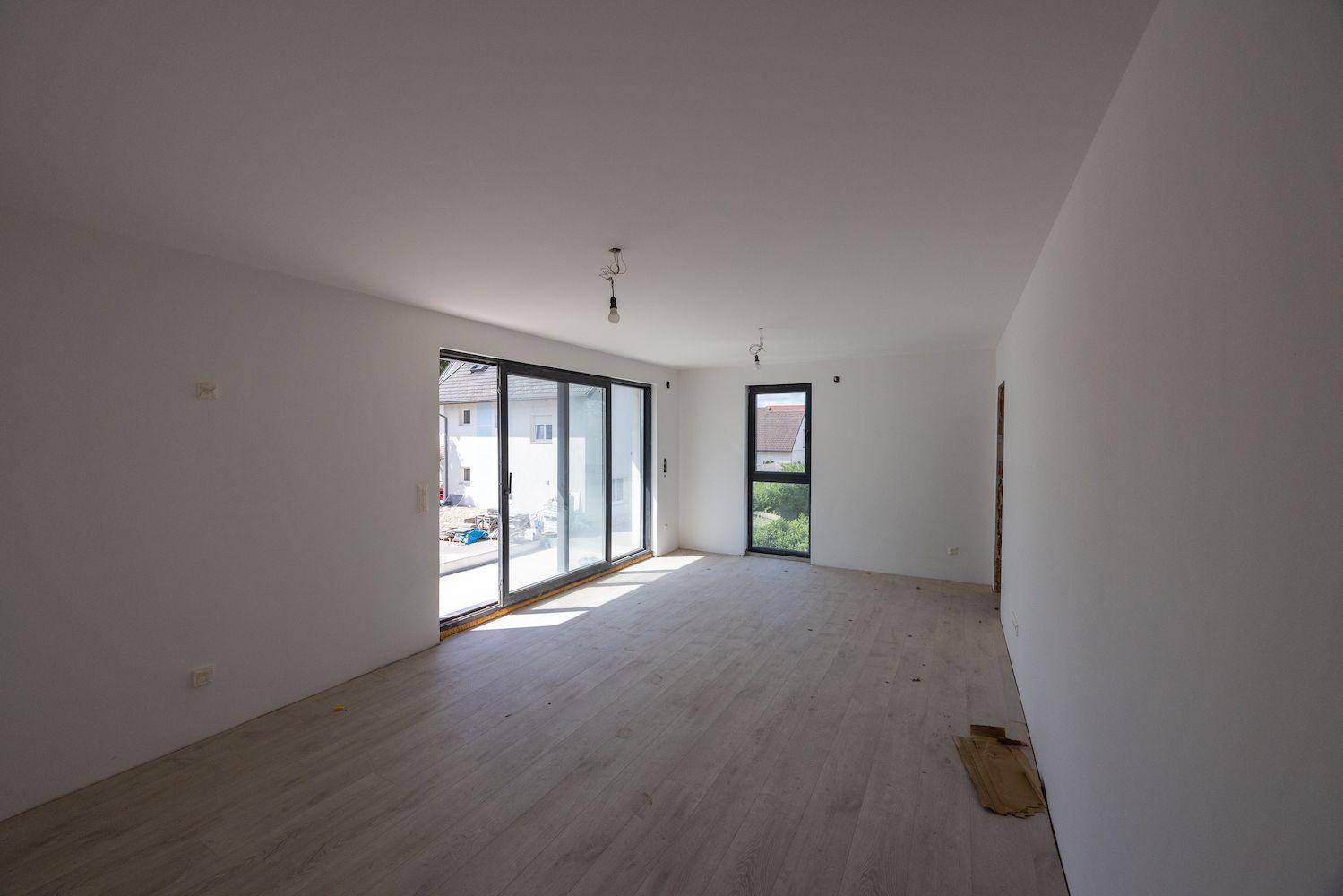 Heller, leerer Wohnraum mit großen Schiebetüren, die viel Tageslicht hereinlassen und Zugang nach draußen bieten.