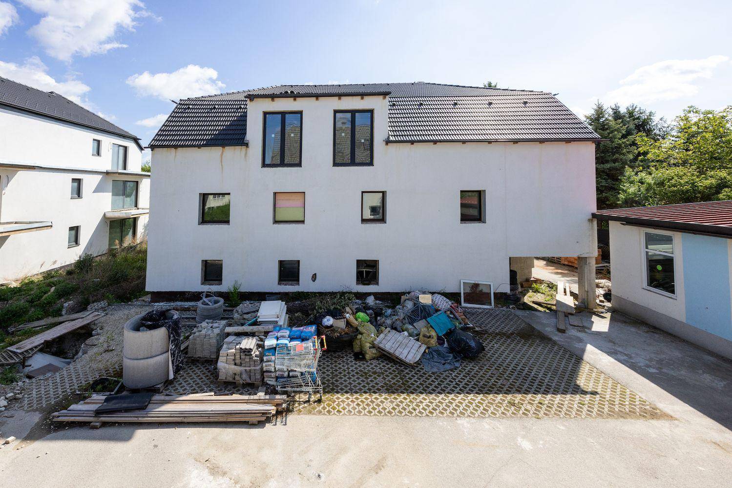 Rückansicht eines im Bau befindlichen Gebäudes mit weißer Fassade und Baustellenmaterialien im Vordergrund.