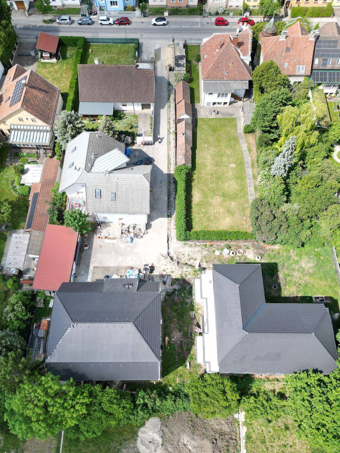 Luftaufnahme einer Wohnsiedlung mit verschiedenen Häusern, Gärten und einem Neubau mit dunklem Dach.