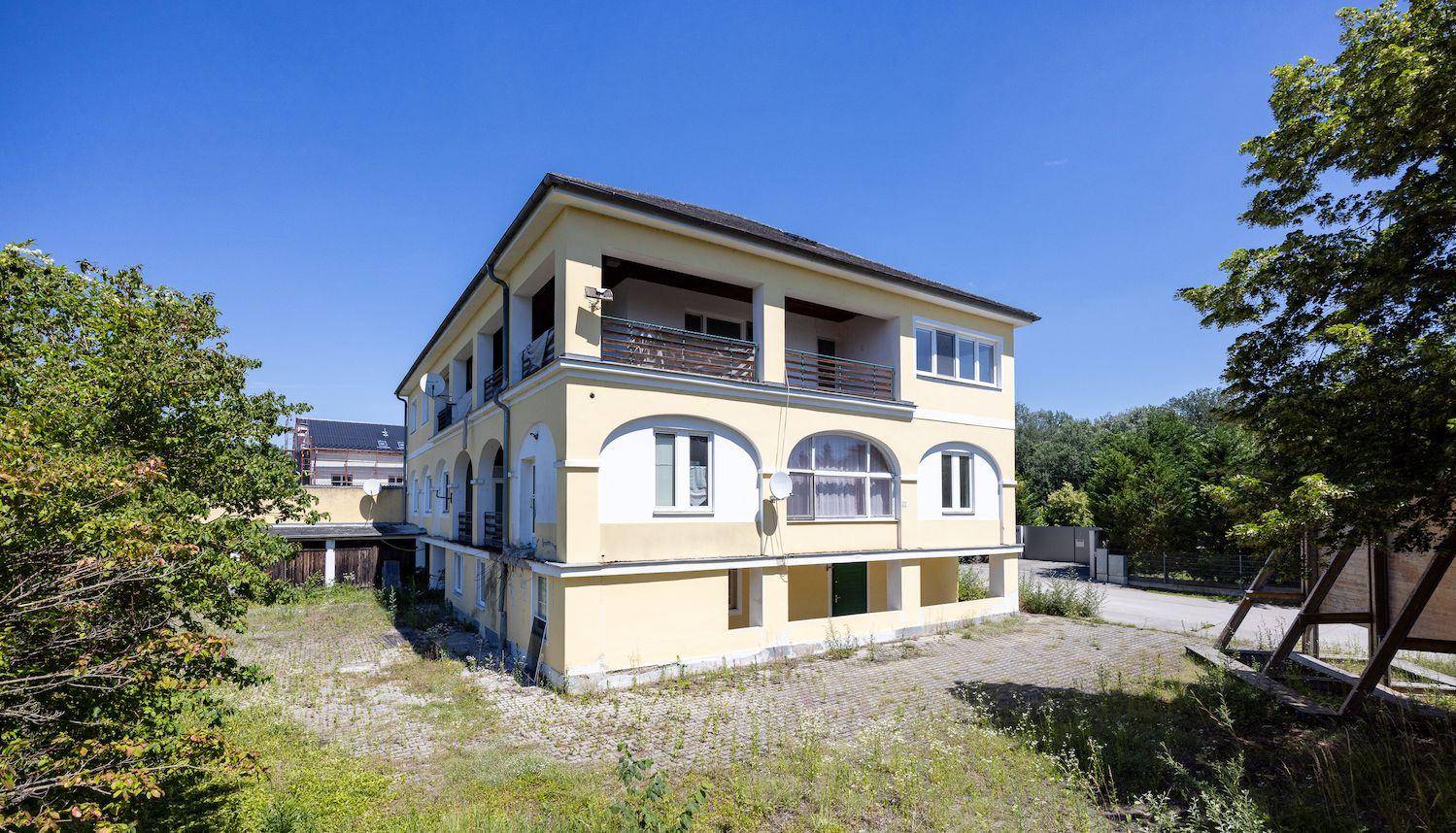 Gelbes Mehrfamilienhaus mit Balkonen und großen Fenstern, umgeben von viel Grün und Bäumen.