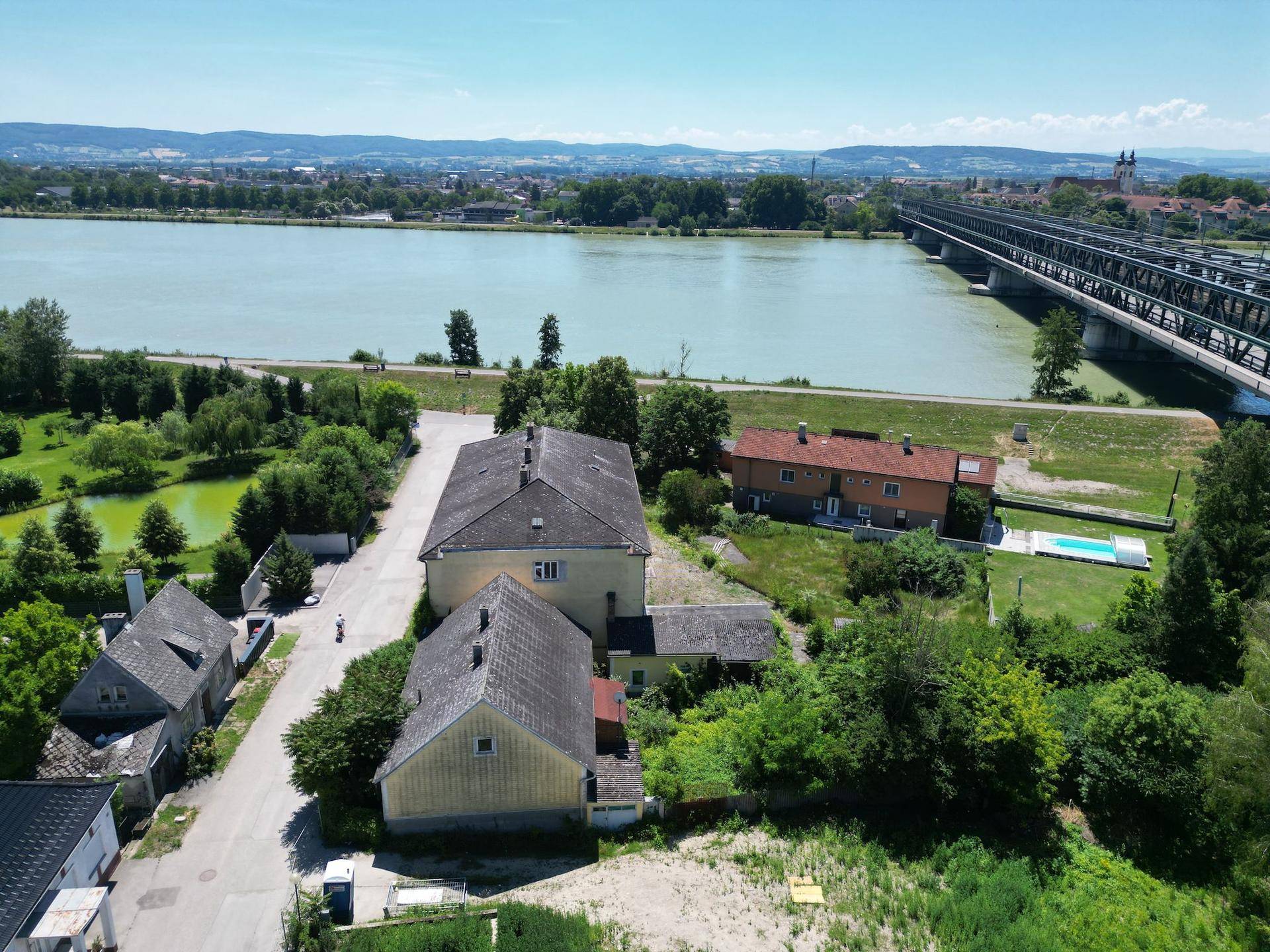 Luftaufnahme des Anwesens mit mehreren Gebäuden, einem Fluss und einer Brücke im Hintergrund.