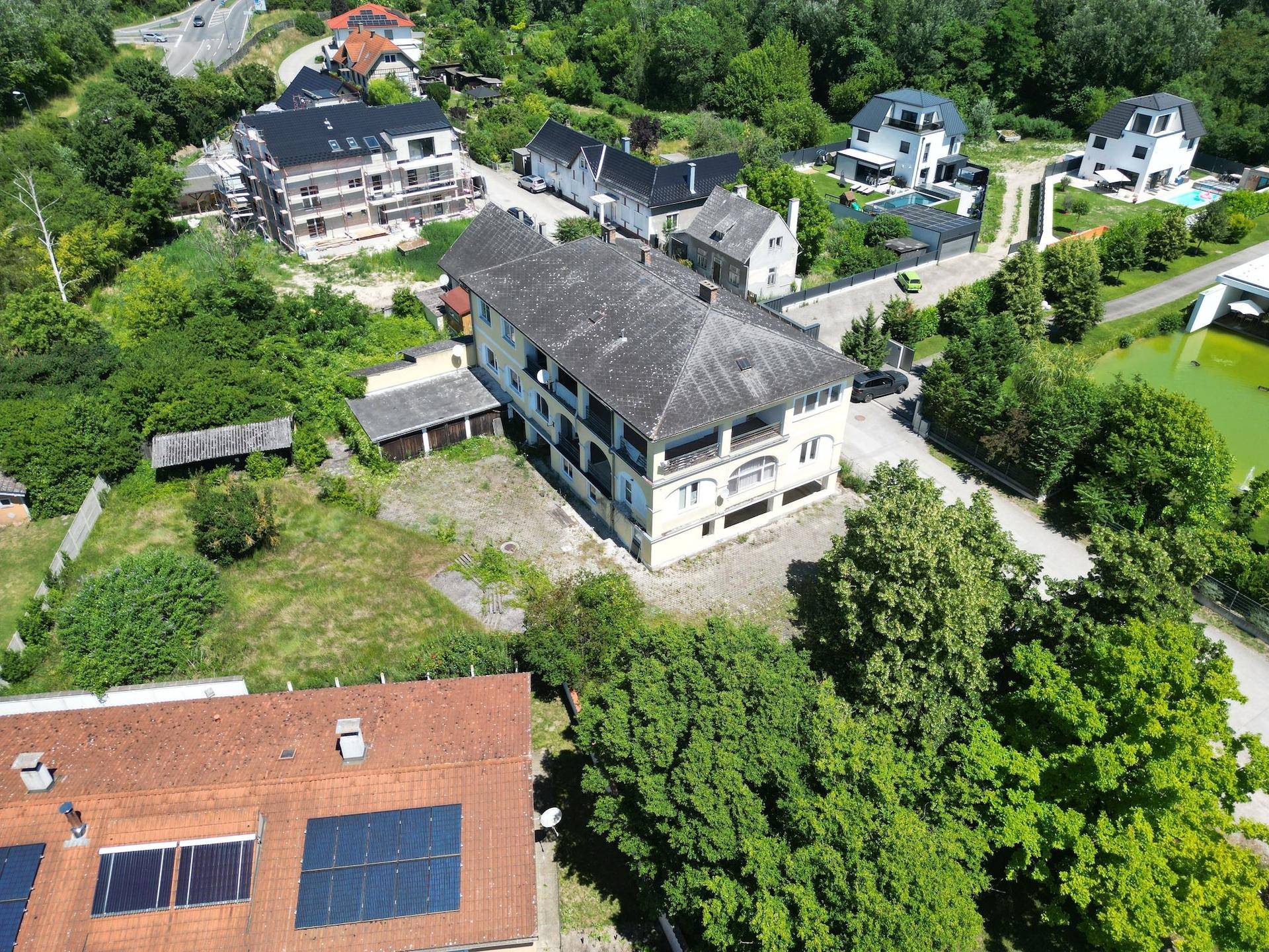 Luftaufnahme des Anwesens mit dem Hauptgebäude, umgeben von Bäumen und weiteren Häusern.