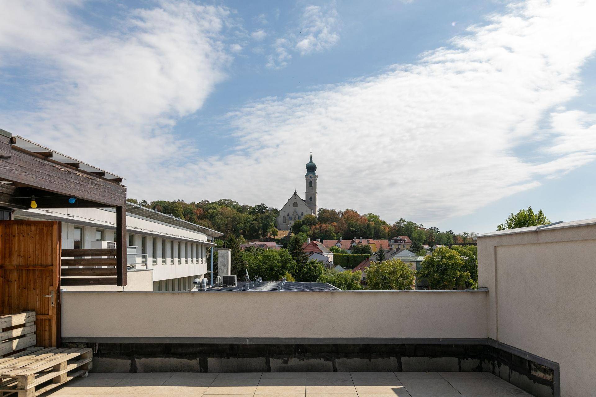 Geräumige Dachterrasse mit weitem Blick über die Stadt und eine Kirche im Hintergrund.