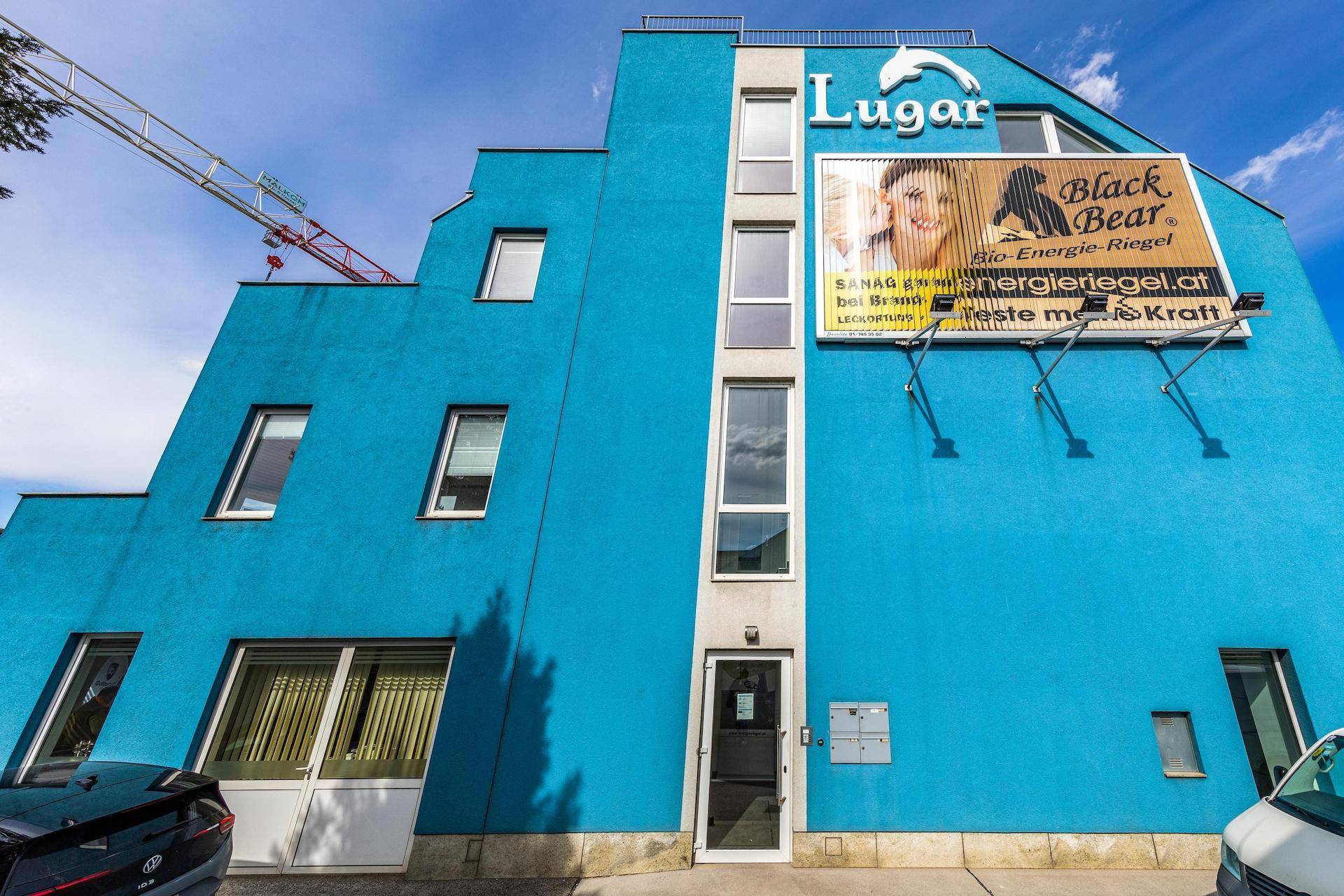 Eingangsbereich eines modernen blauen Gebäudes mit großen Fenstern und Werbetafeln an der Fassade.