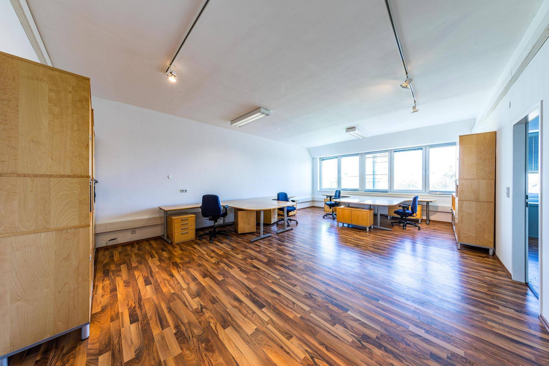 Geräumiges, helles Büro mit Holzfußboden, mehreren Arbeitsplätzen und großen Fenstern.