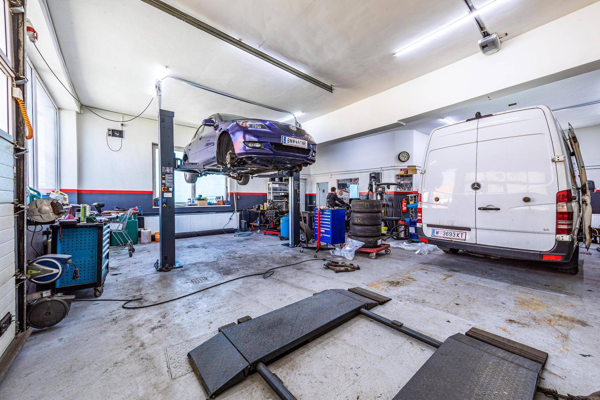 Werkstatt mit Hebebühne, auf der ein Auto repariert wird, und verschiedenen Werkzeugen.