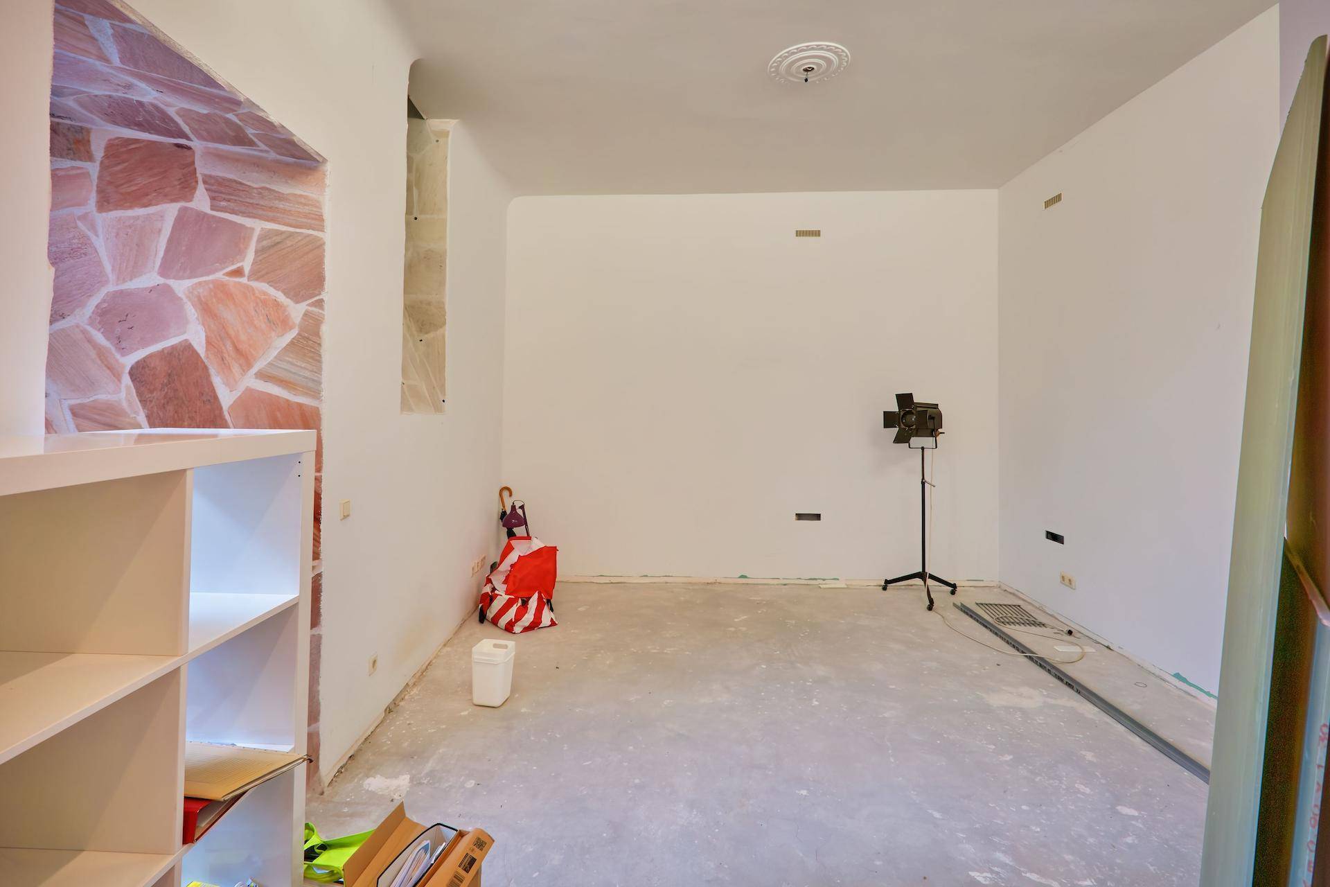 Leerer Raum in Renovierung mit weißen Wänden, Betonboden und einer Wandverkleidung aus Naturstein.