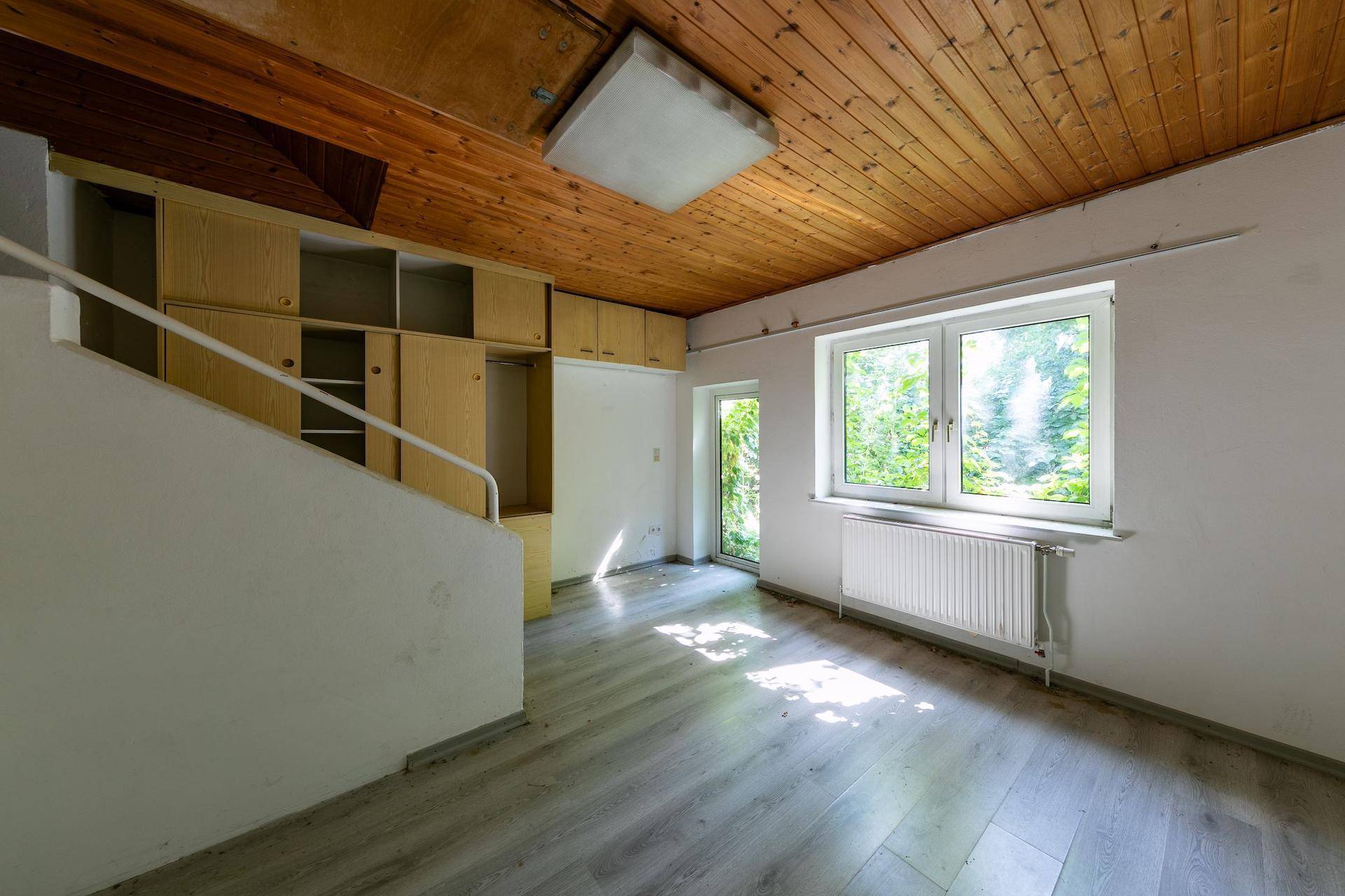 Raum mit Holzdecke, Einbauschränken und Zugang zu einem Außenbereich durch eine Tür.