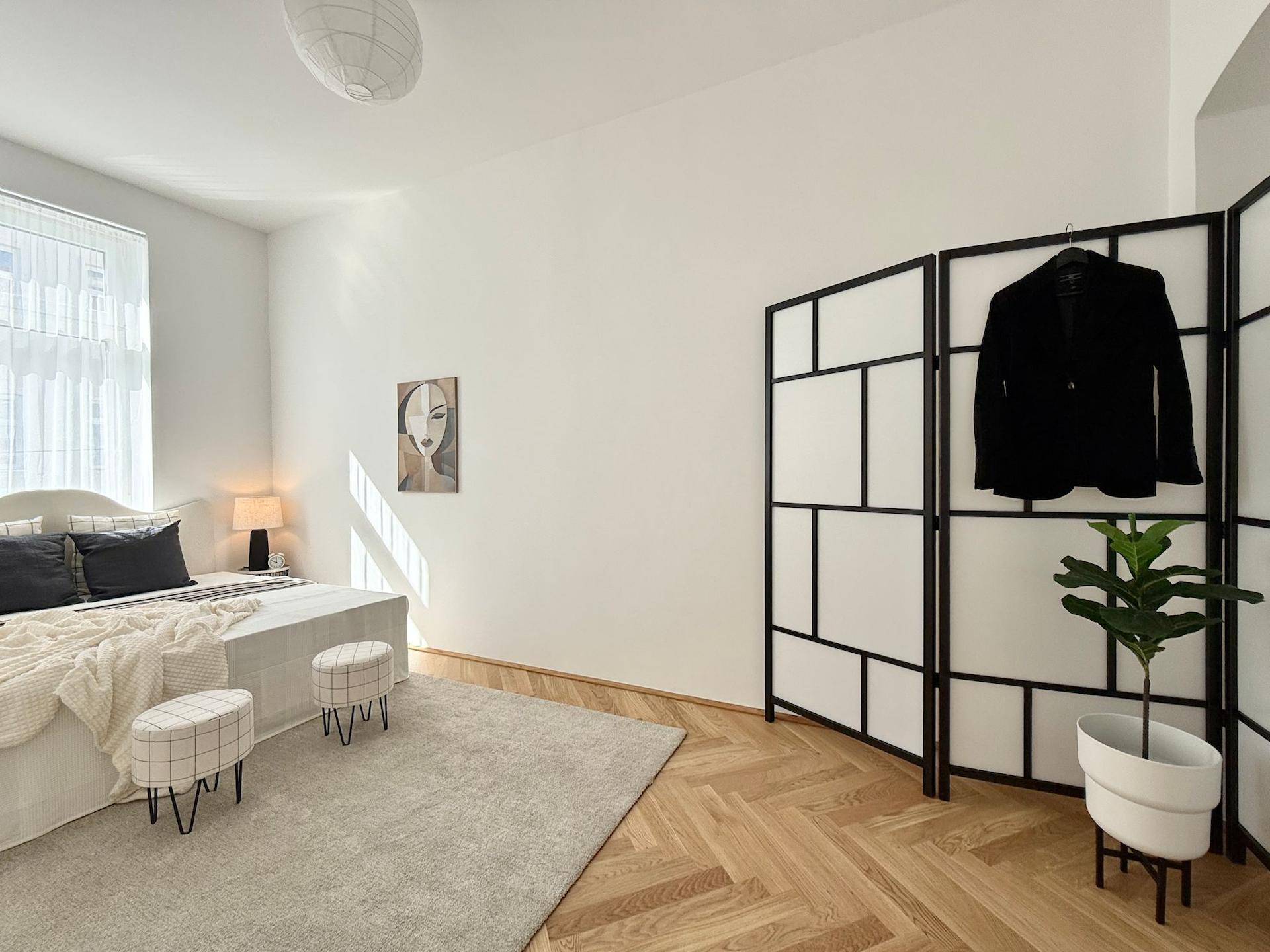 Schlafzimmer mit Fischgrätparkett, minimalistischem Raumteiler und viel Tageslicht.