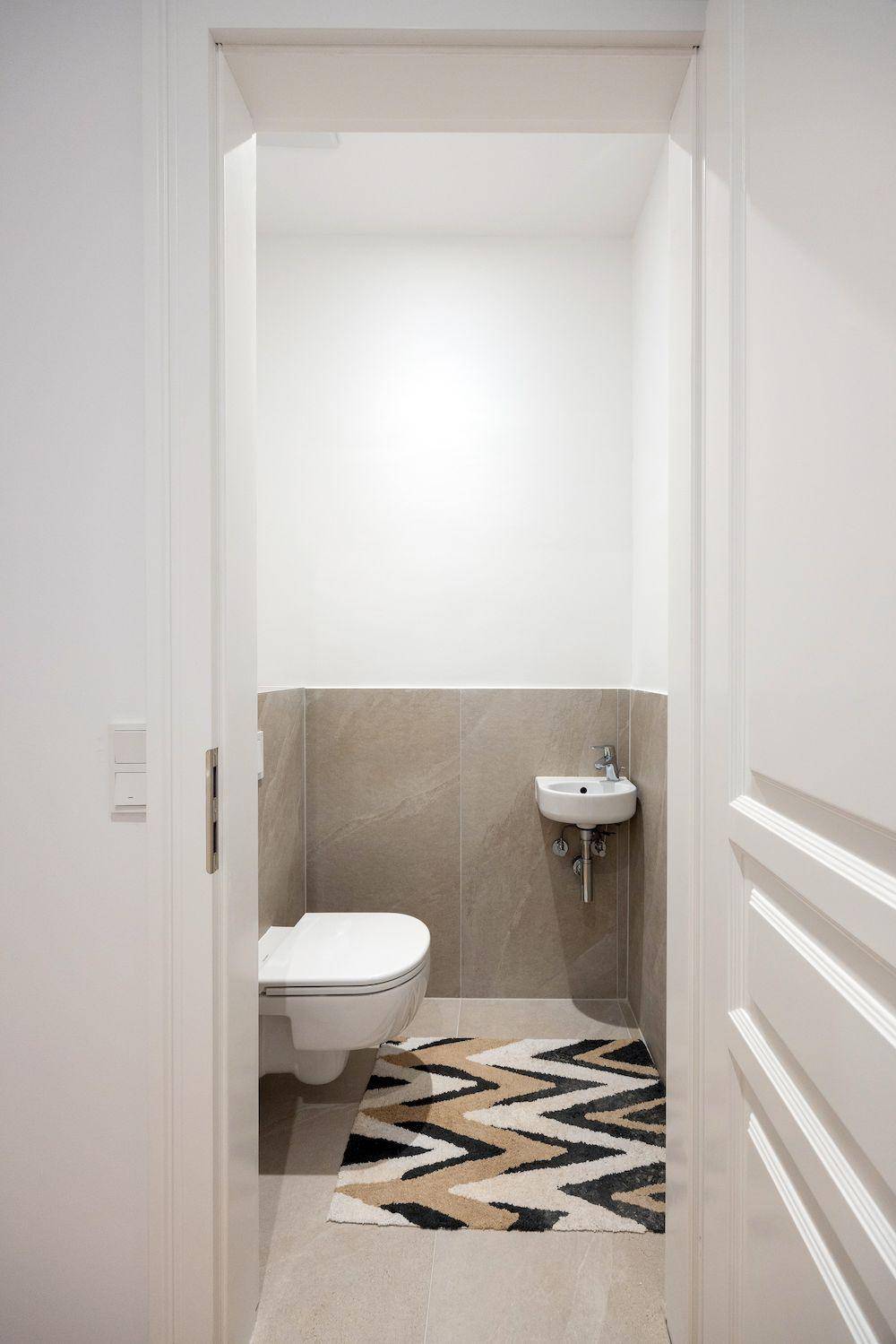 Modernes Gäste-WC mit Wand-WC, kleinem Waschbecken und gemustertem Teppich.