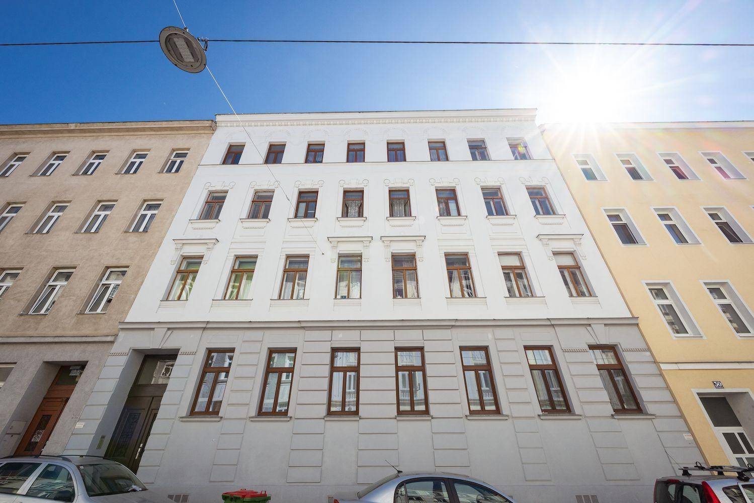 Sonnenbeschienene Fassade eines Mehrfamilienhauses mit klassischer Architektur und vielen Fenstern.
