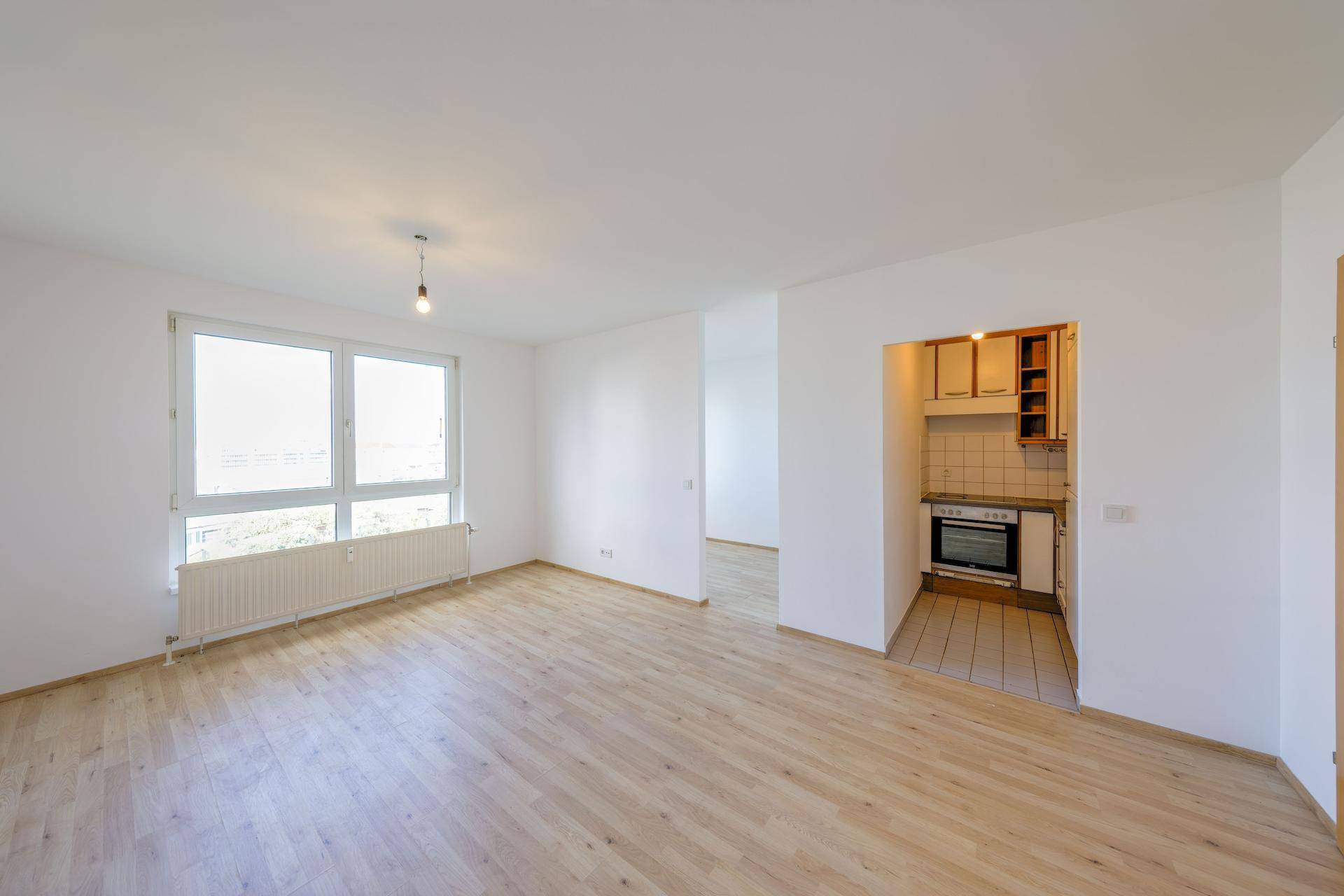 Geräumiges, leeres Wohnzimmer mit hellem Parkettboden und einer praktischen Küchennische.
