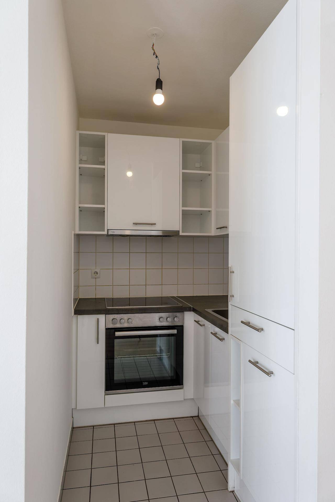 Funktionale Küchenzeile mit weißen Hochglanzschränken, integriertem Backofen und Fliesenboden.