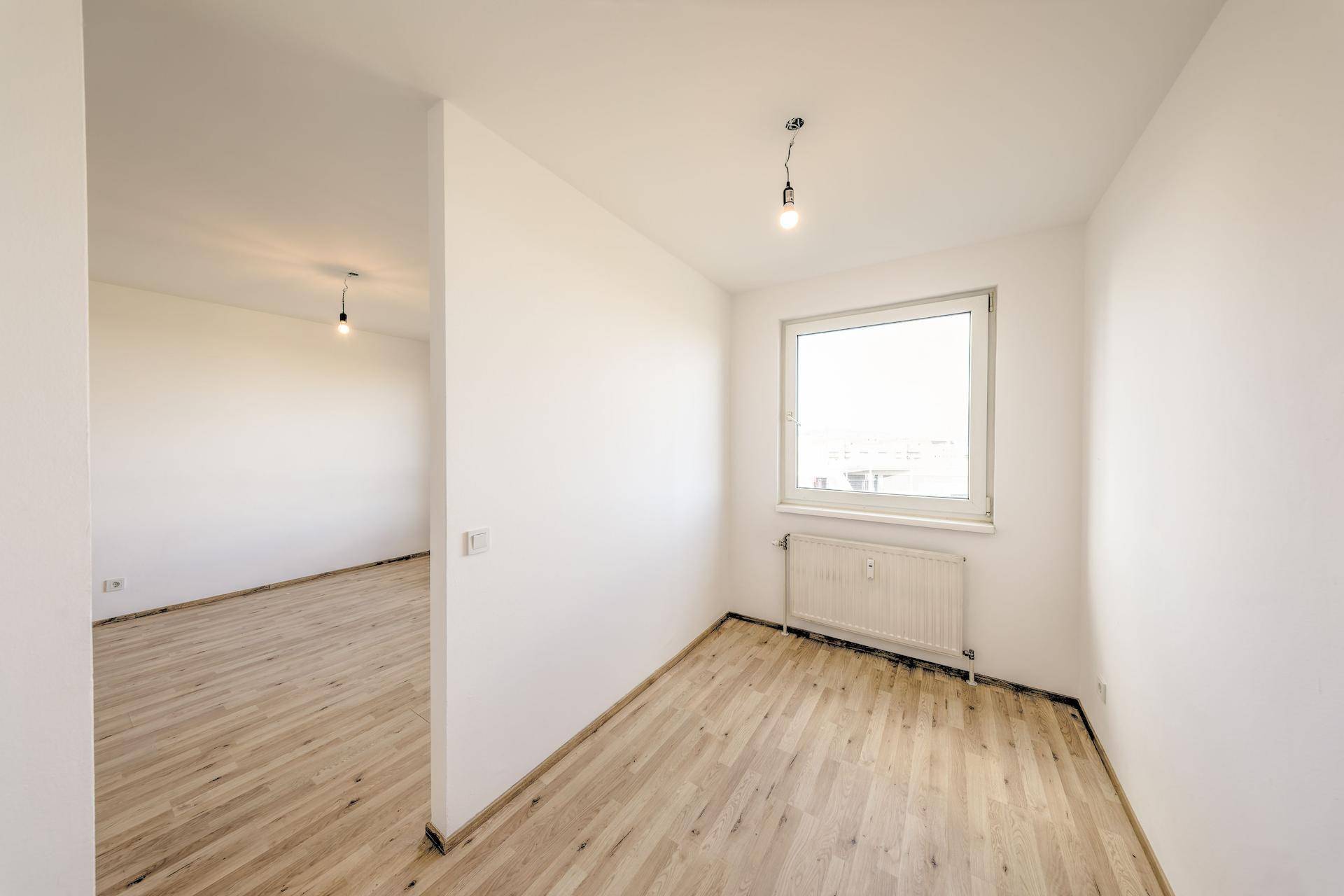 Helles Zimmer mit Laminatboden und einem Fenster, das viel Tageslicht hereinlässt.