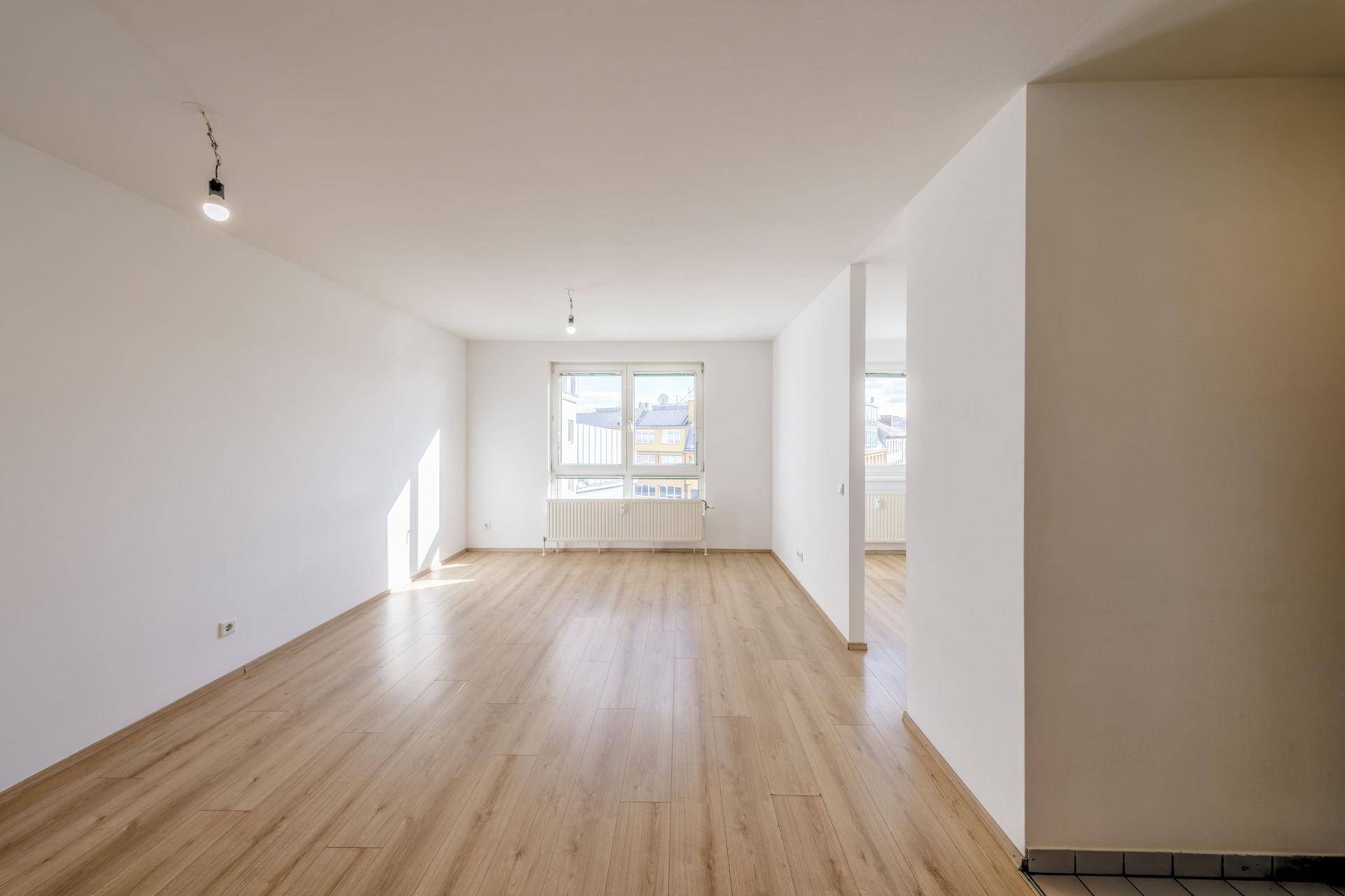 Lichtdurchfluteter Wohnraum mit Laminatboden und Blick auf die Umgebung durch große Fenster.
