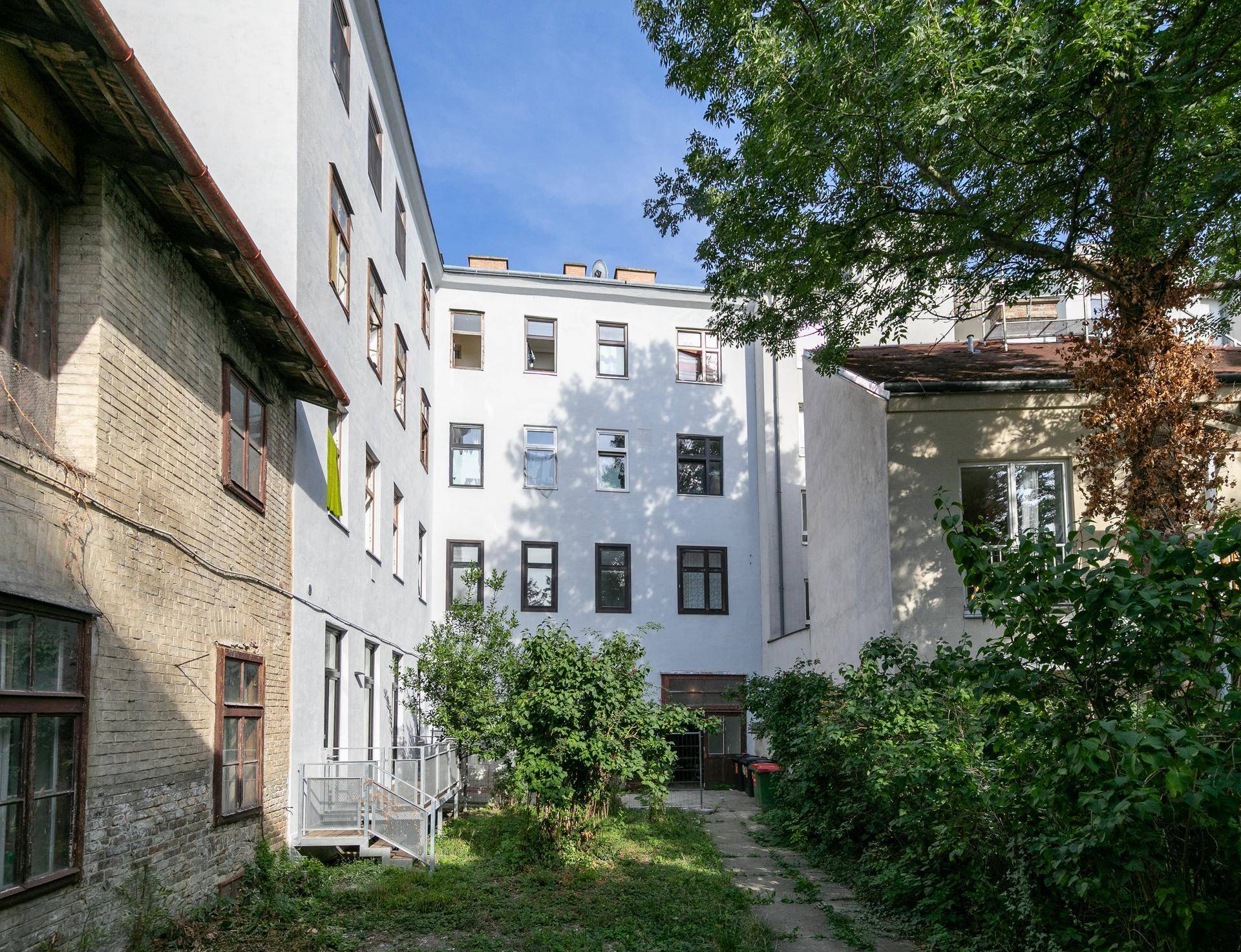 Innenhof eines Wohngebäudes mit Grünflächen, Bäumen und Zugang zu den Wohnungen.