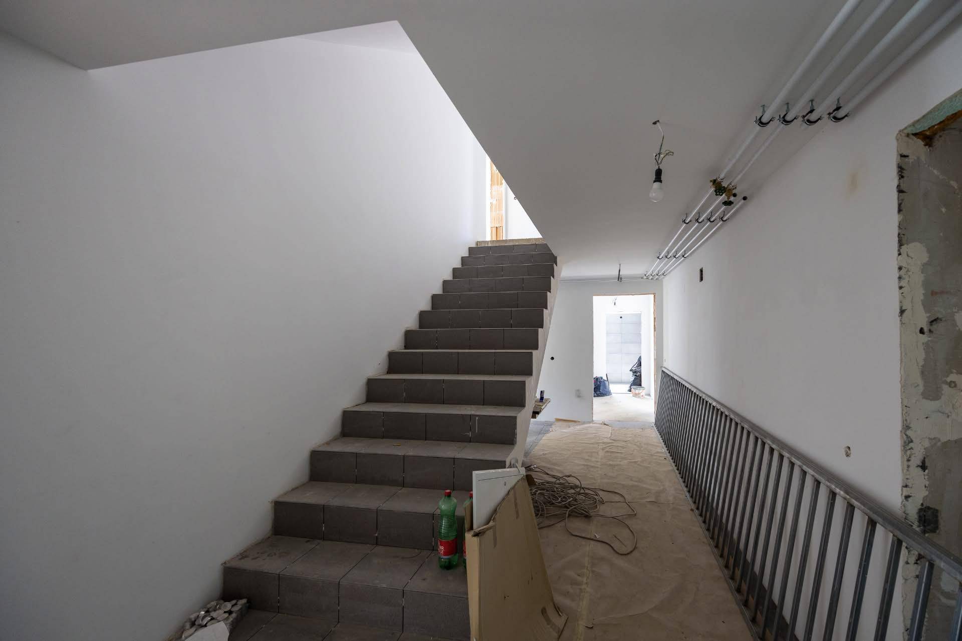 Treppenhaus im Rohbau mit Steinstufen und einem Geländer, das zu den oberen Etagen führt.