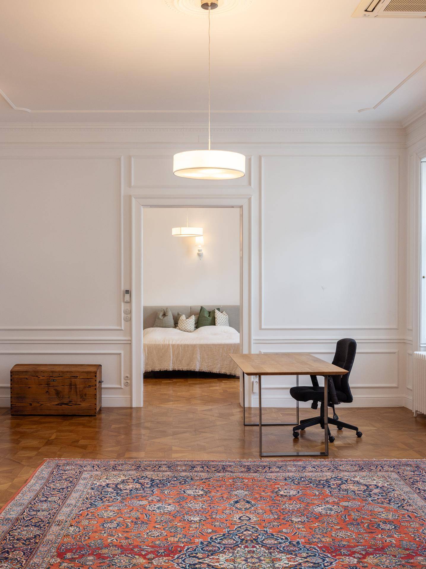 Geräumiger Wohnbereich mit Arbeitsplatz und Zugang zu einem angrenzenden Schlafzimmer.