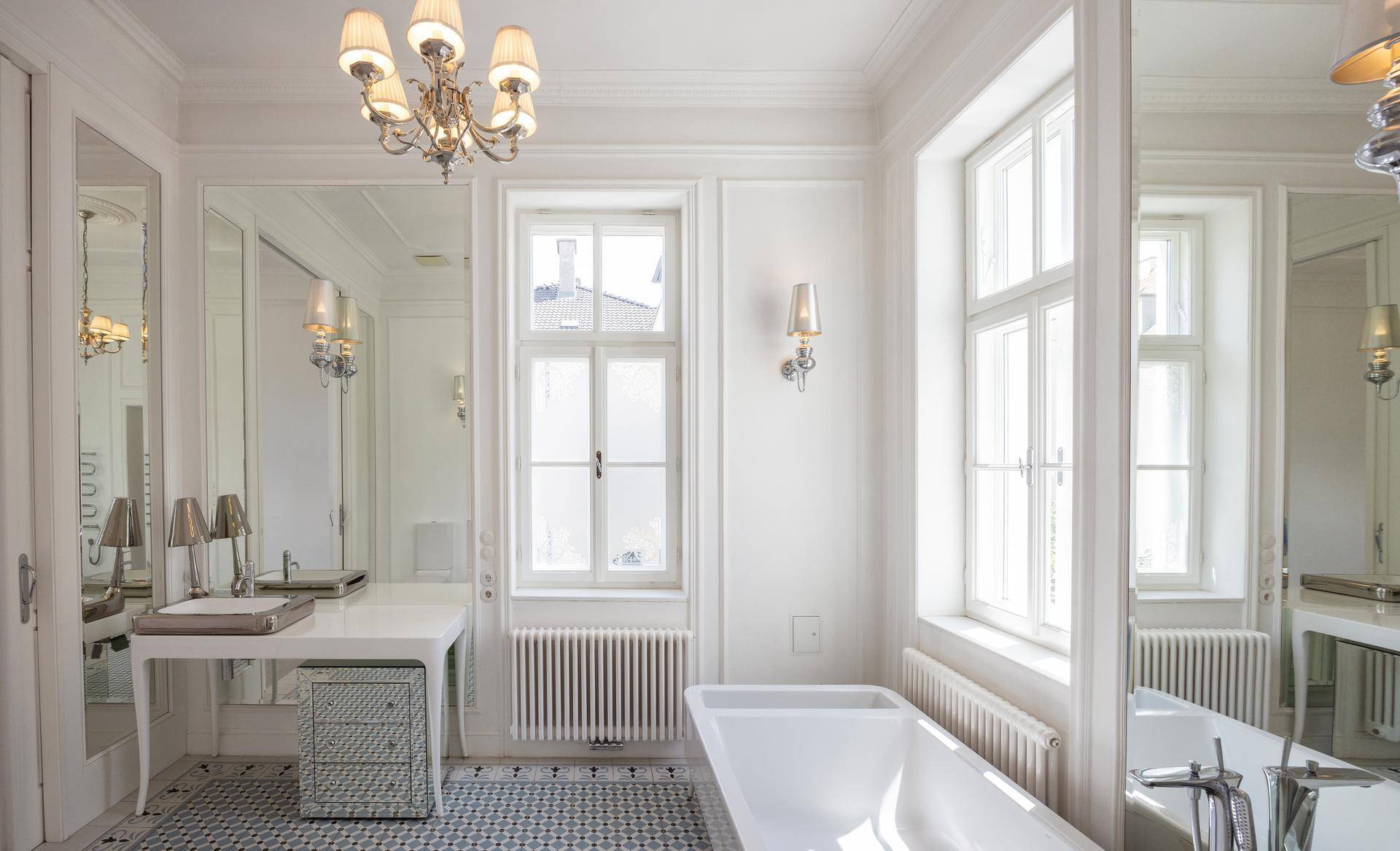 Helles Badezimmer mit stilvollem Waschtisch, großen Spiegeln und freistehender Badewanne.