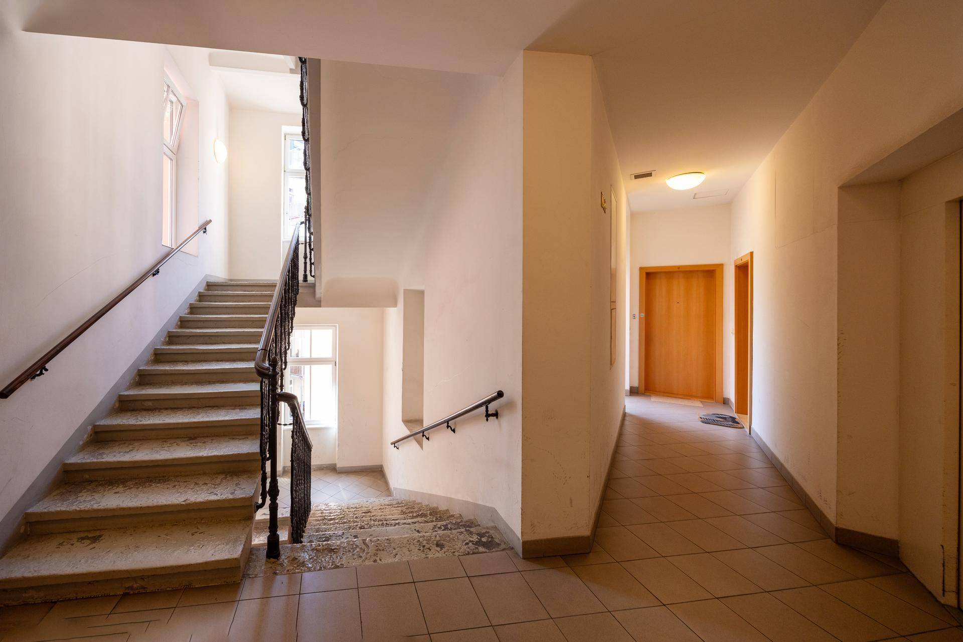 Geräumiger Hausflur mit breiter Steintreppe, Fliesenboden und Zugangstüren zu den Wohnungen.