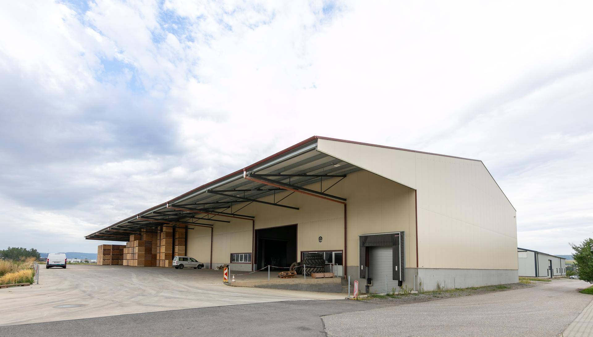 Ansicht der modernen Lagerhalle mit großen Rolltoren und überdachtem Bereich, umgeben von einer weiten Fläche.