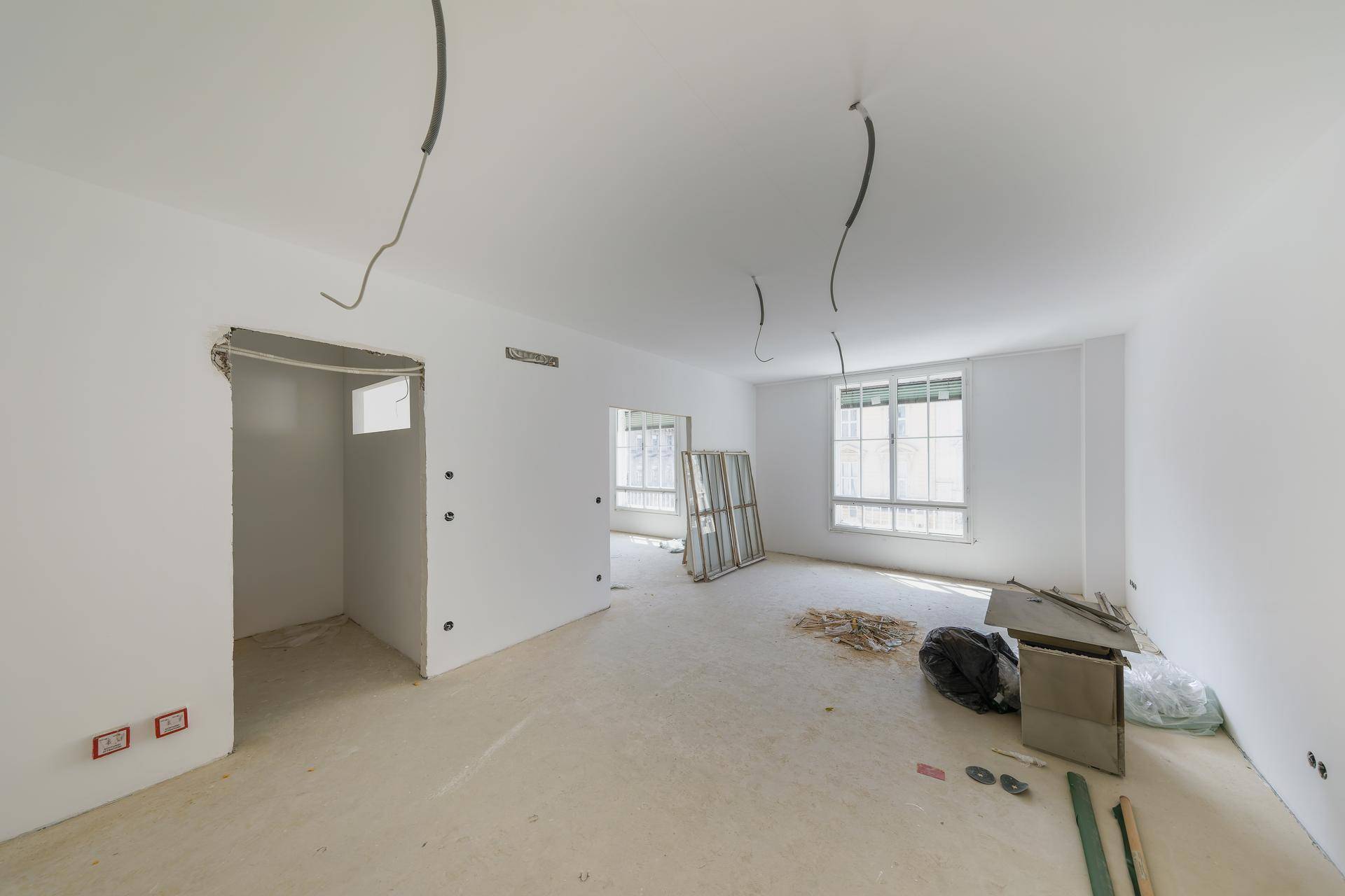 Unfertiger Innenraum mit weißen Wänden, Betonboden und sichtbaren Kabeln während der Renovierung.
