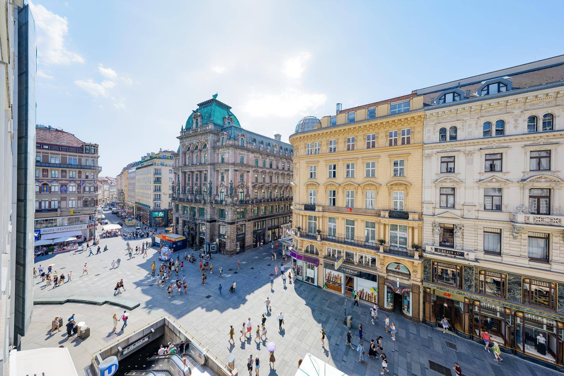 Panoramablick auf einen belebten Stadtplatz mit eleganter Architektur und vielen Passanten.
