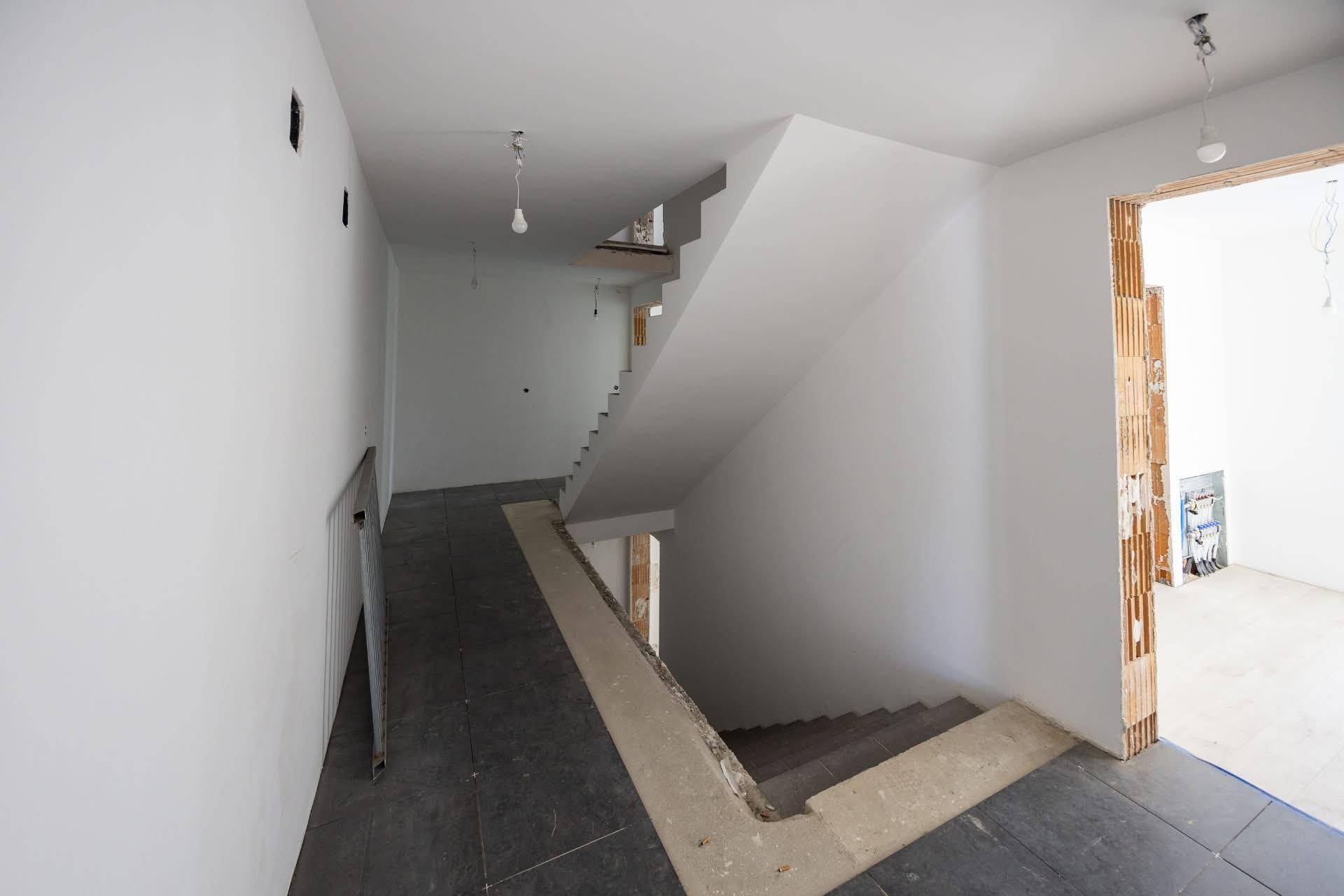 Treppenhaus im Rohbau mit dunklen Fliesen und einer Rampe, die zu den oberen Etagen führt.